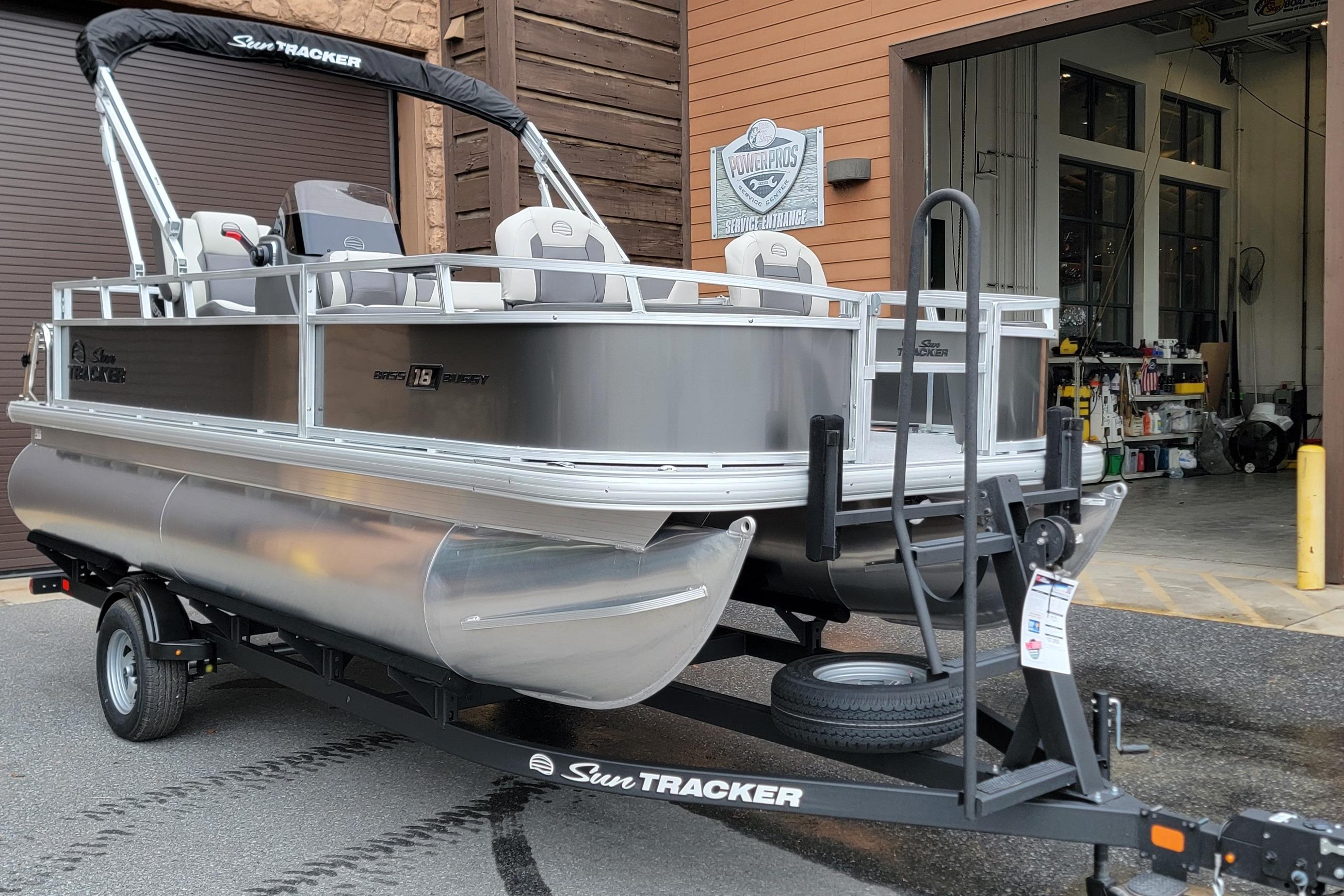 2026 Sun Tracker Bass Buggy 18 DLX pontoon boat on trailer outside service entrance.