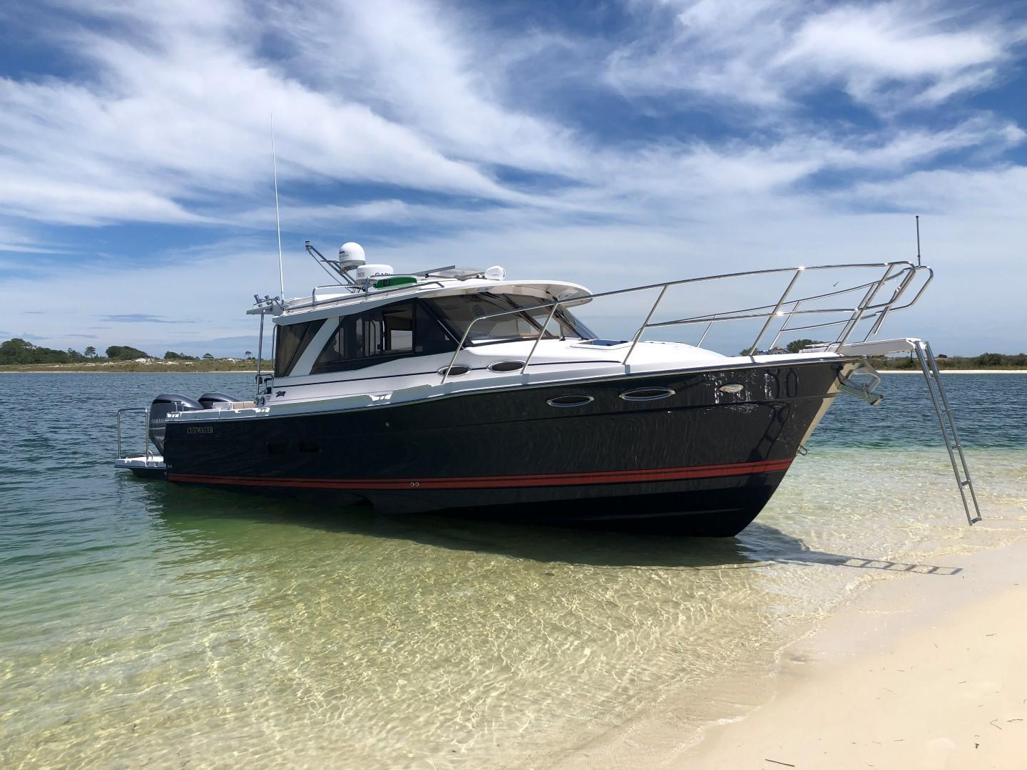 2025 Cutwater C-32 Sedan boat on sandy shore under blue sky.