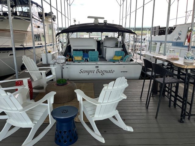 A 1989 Trojan 370 Express docked under a covered area. White chairs and a table are on the deck.