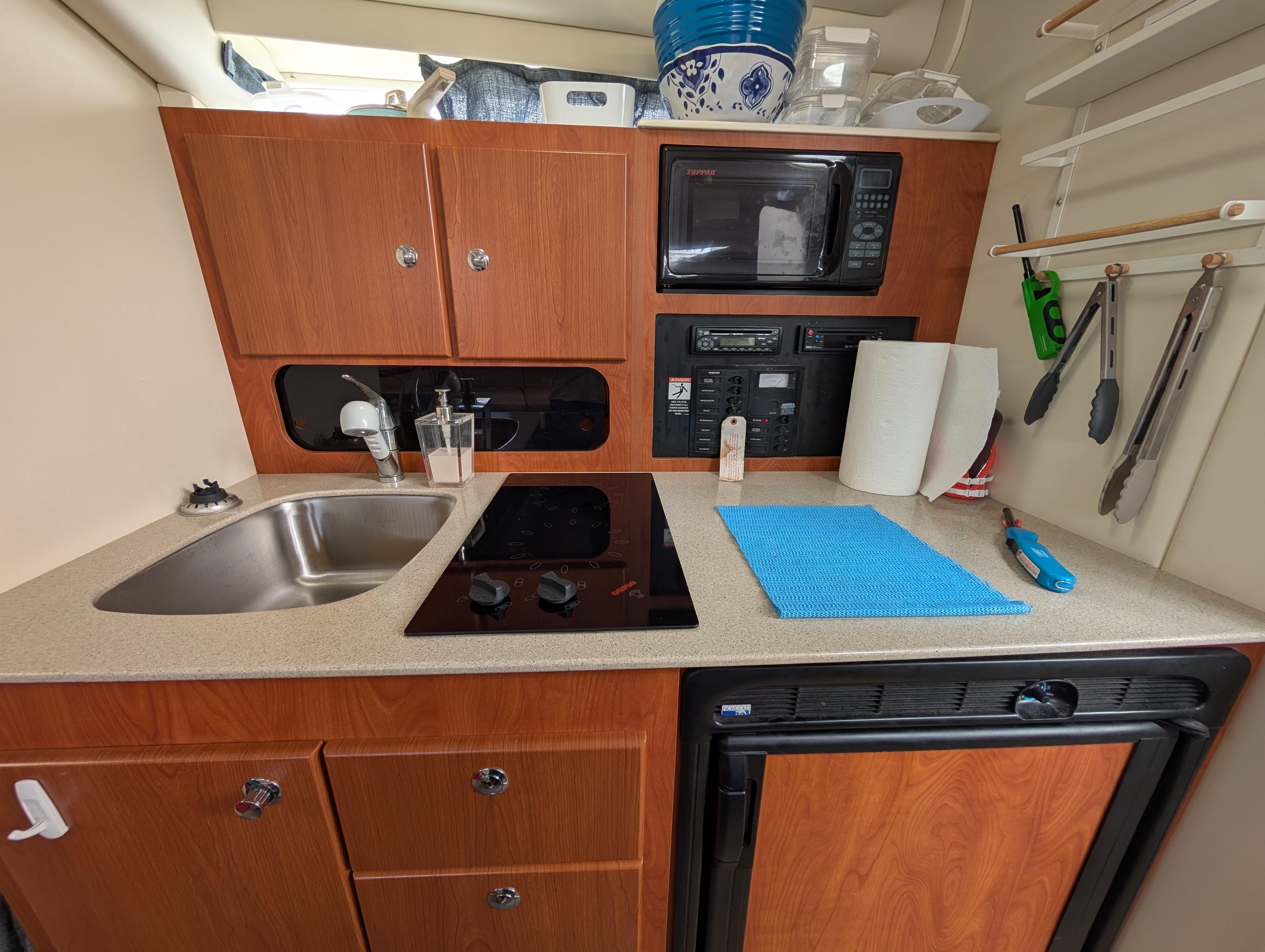 2006 Bayliner 325 boat kitchen with sink, stove, microwave, and storage cabinets.