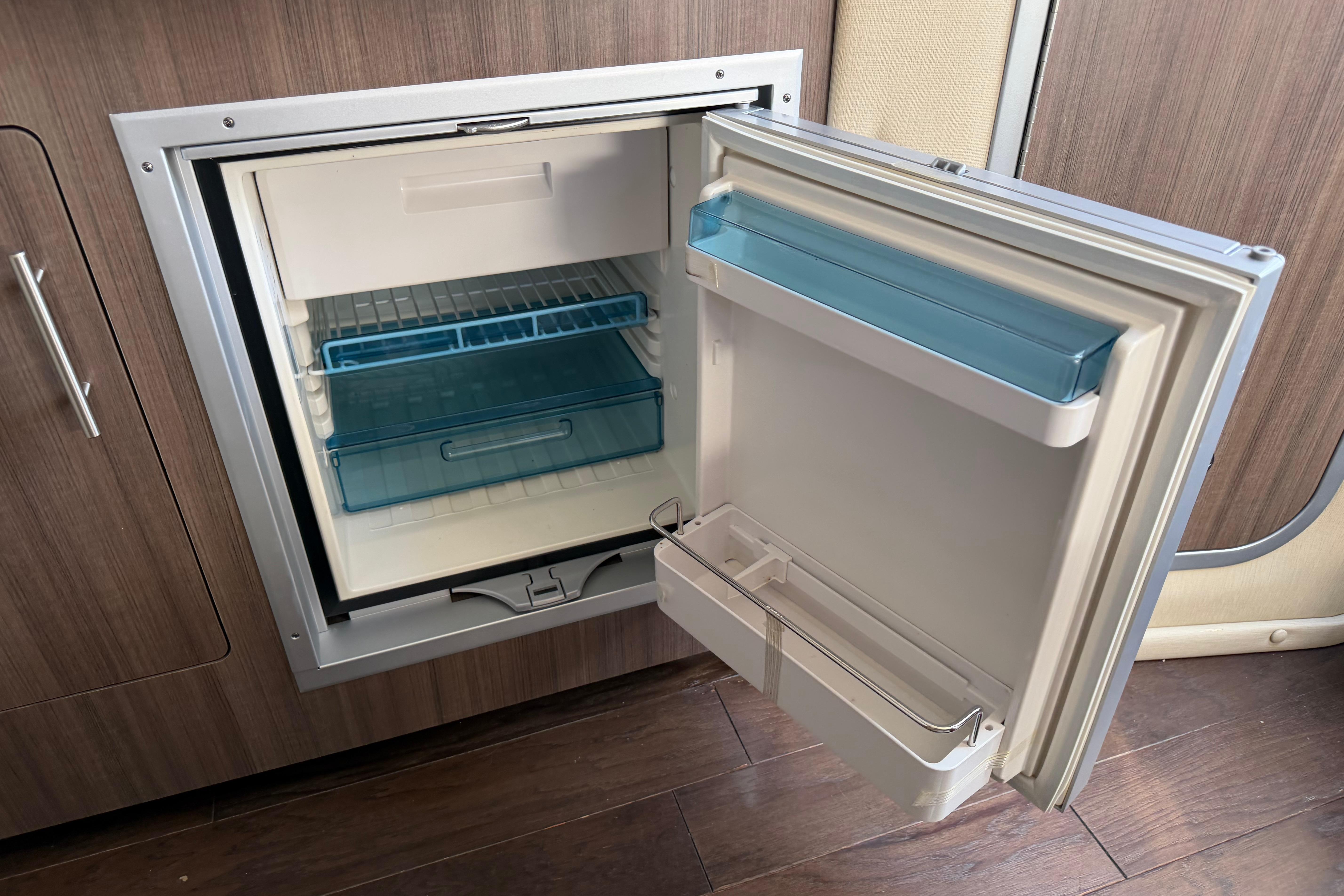 Open refrigerator in 2019 Rinker EX 320 boat, showcasing interior storage compartments.