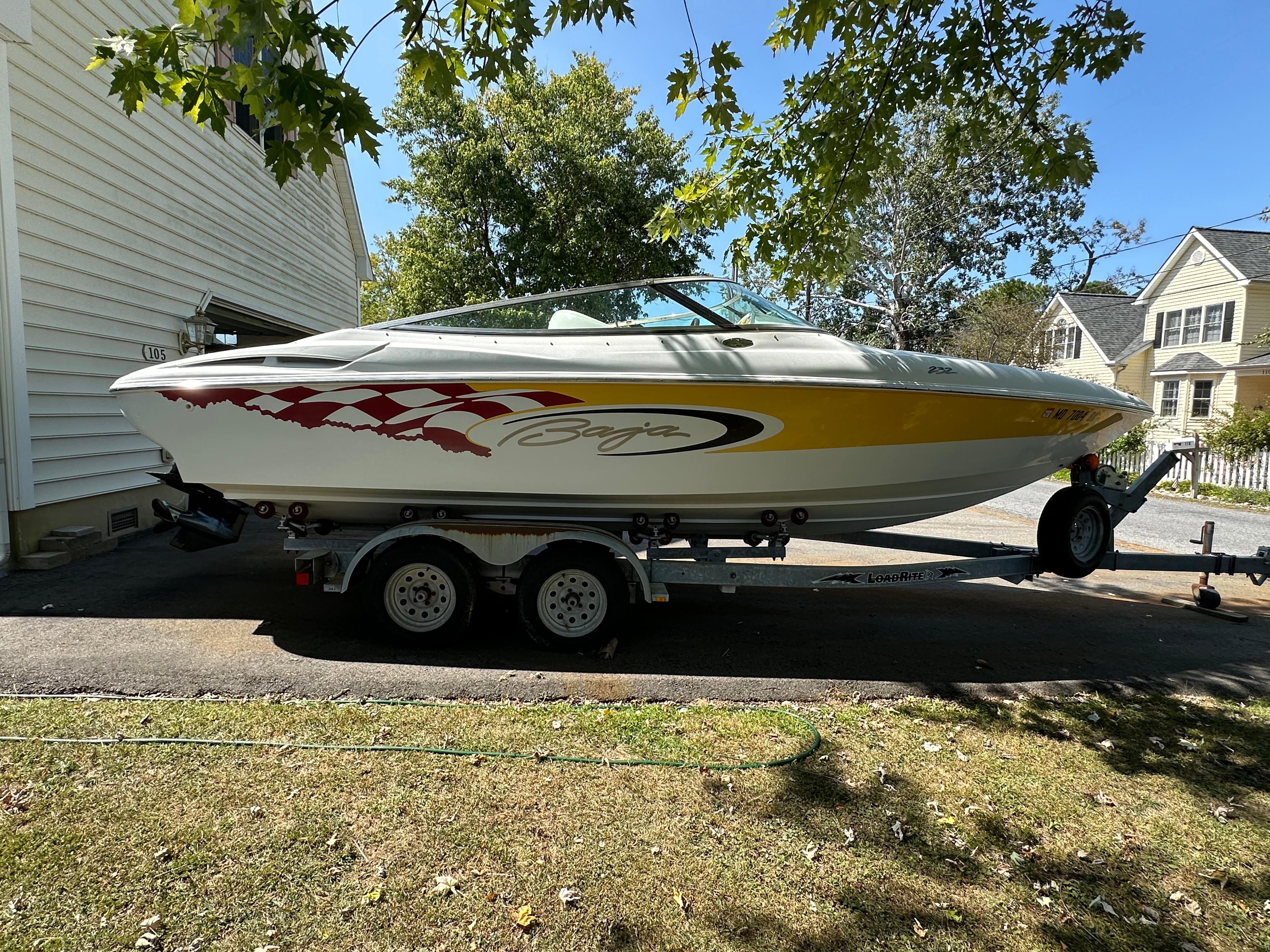 2001 Baja 232 speedboat on trailer, parked in driveway, surrounded by trees and houses.