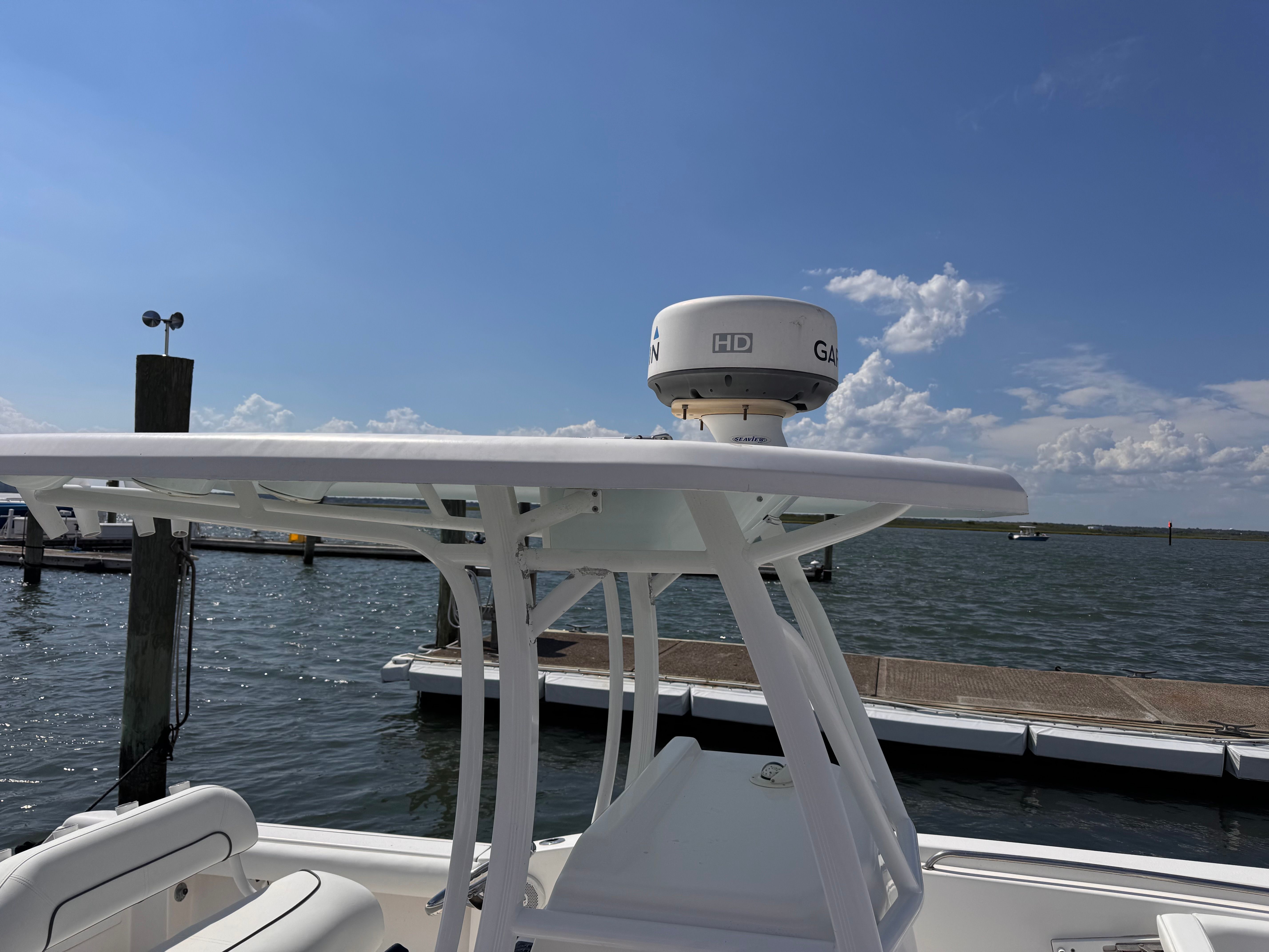 A boat with a white roof and radar on a sunny day at the dock.