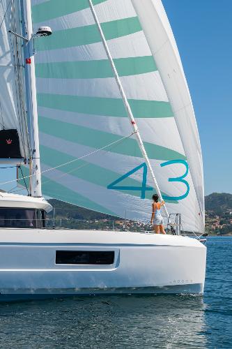 2025 Lagoon 43 sailboat with striped sails on calm water.
