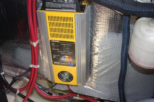 A battery charger is mounted in an engine room, surrounded by cables and insulation.