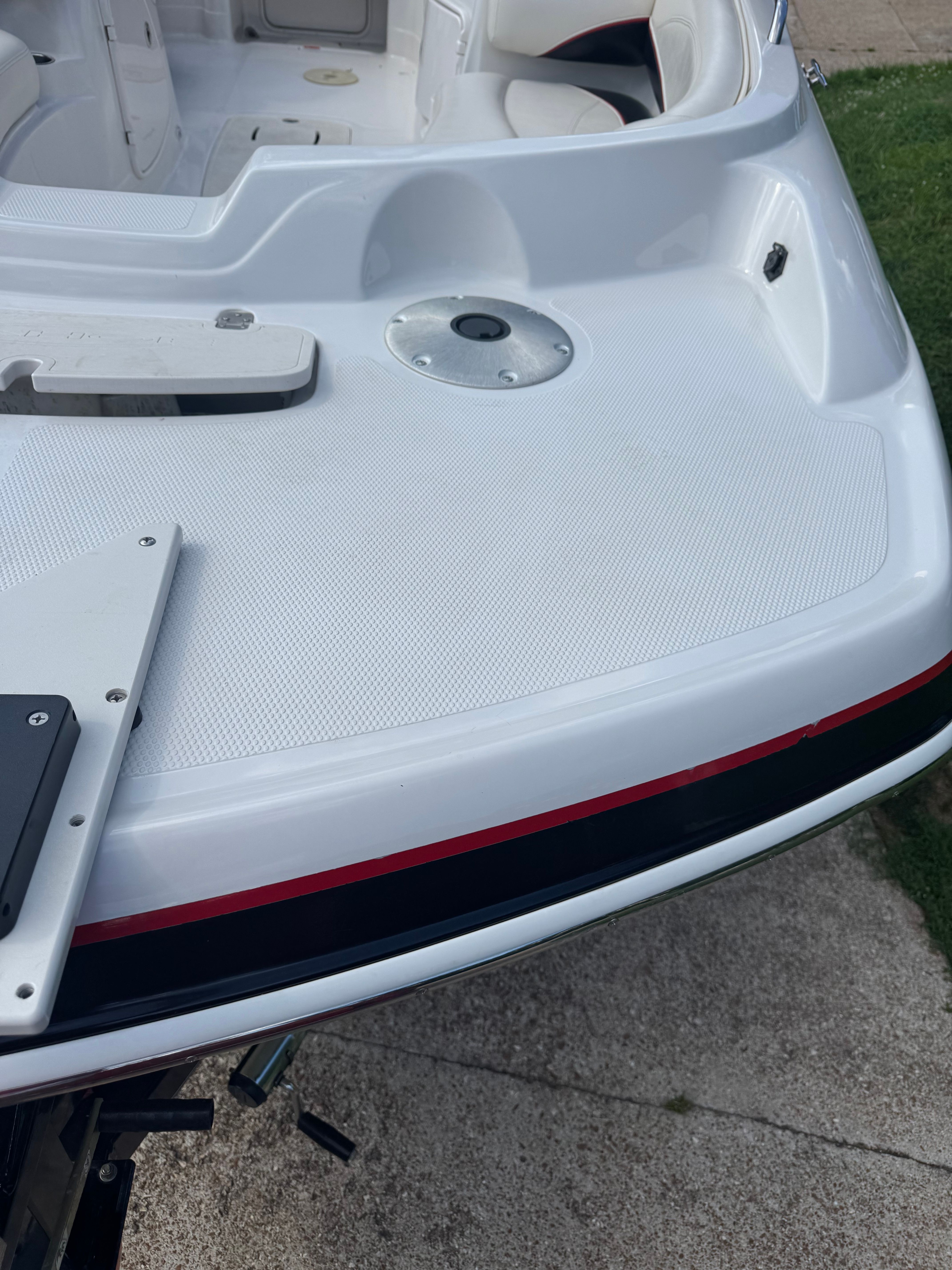 The image shows the stern of a white boat with red accents and a textured deck.