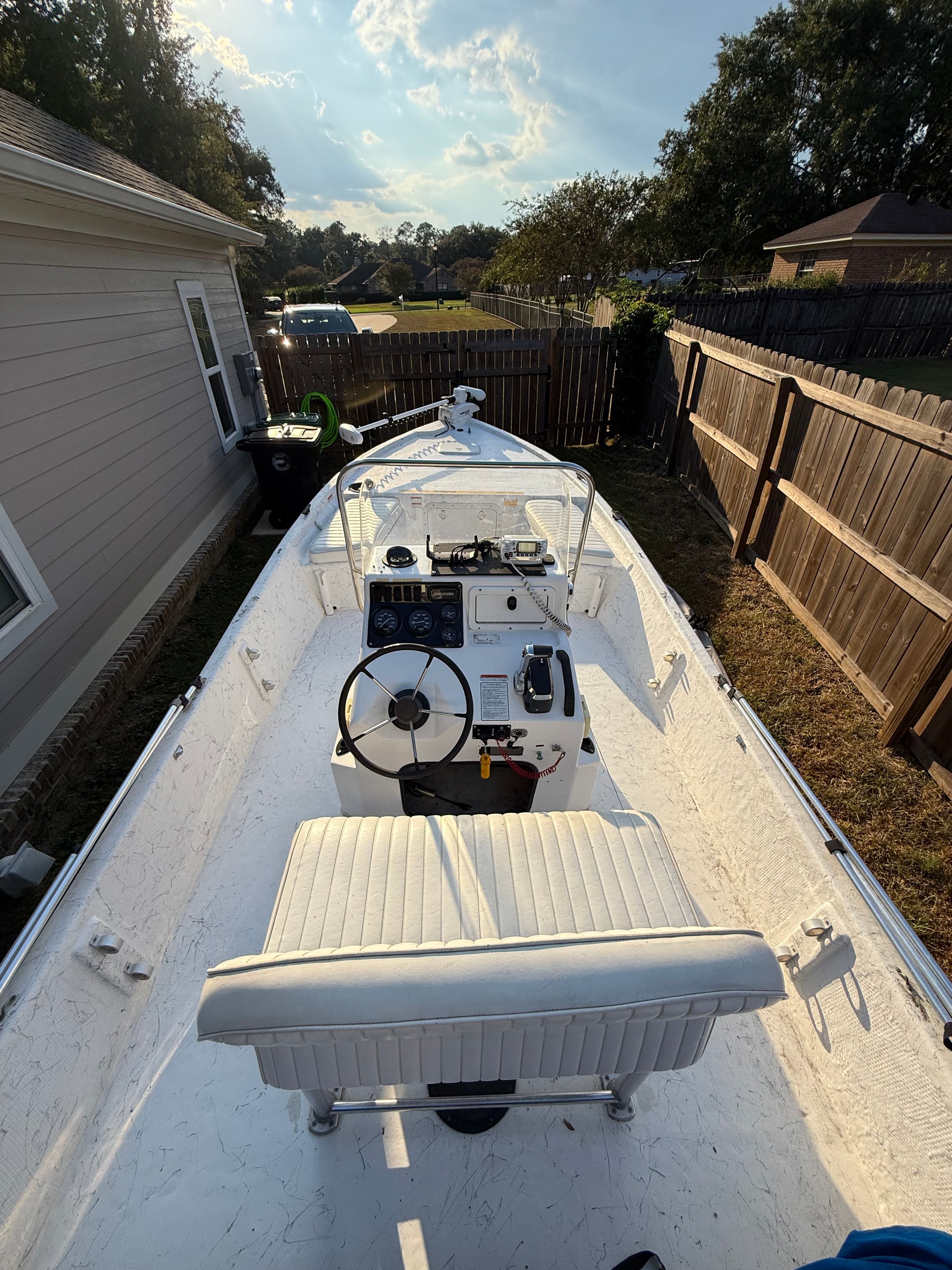 A white boat is parked in a yard next to a house.