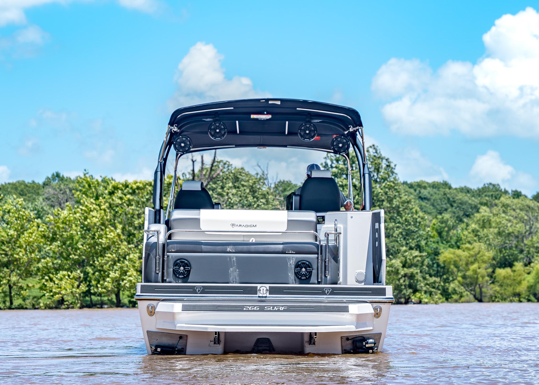 2025 Paradigm Damascus 266 Surf boat on a lake, surrounded by trees and blue sky.