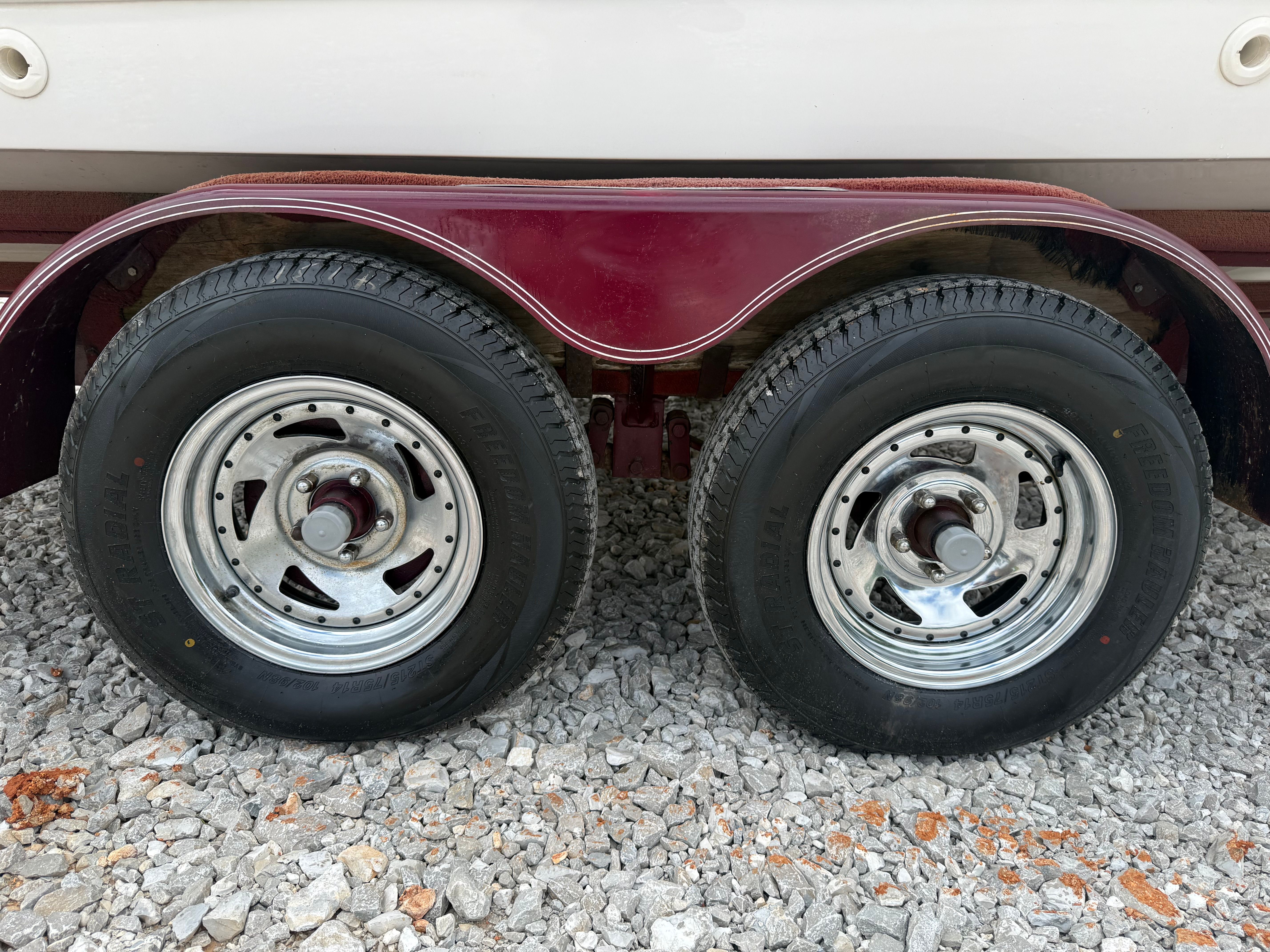 Close-up of a boat trailer with two tires on gravel.