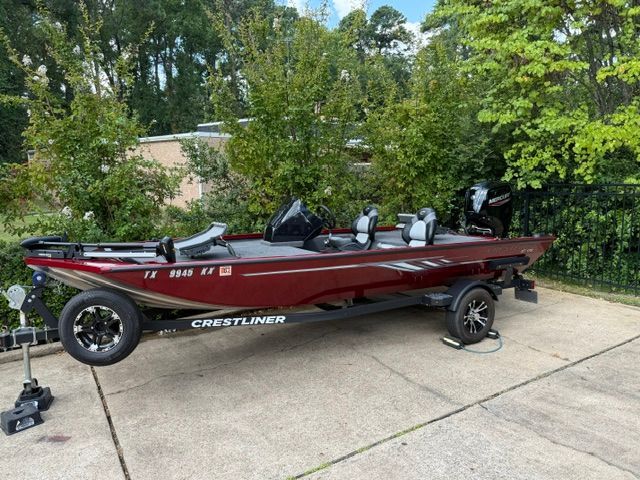 A red 2024 Crestliner XF 179 boat on a trailer in a green setting.
