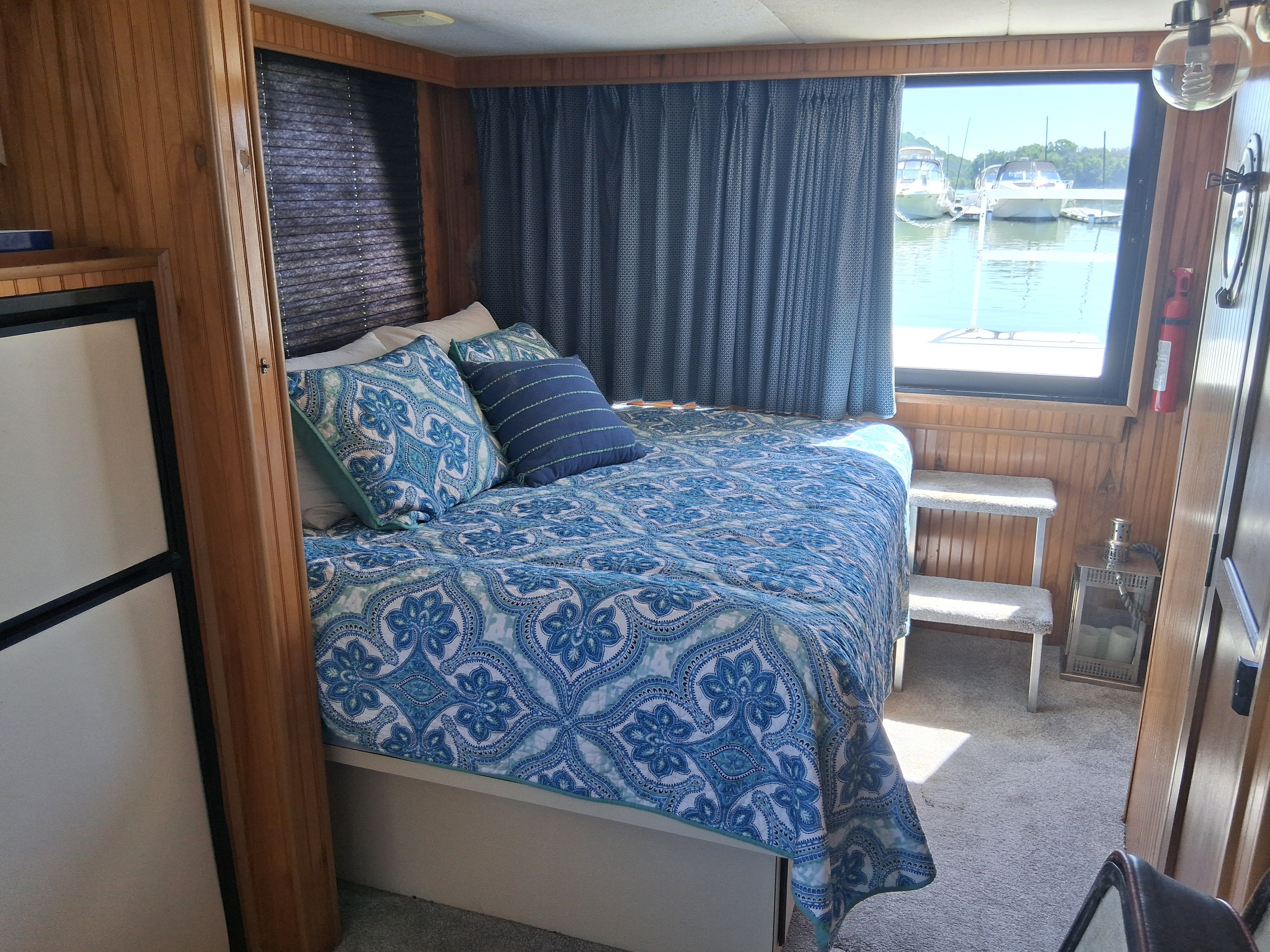 The image shows a cozy bedroom on a boat with a large bed and blue curtains.