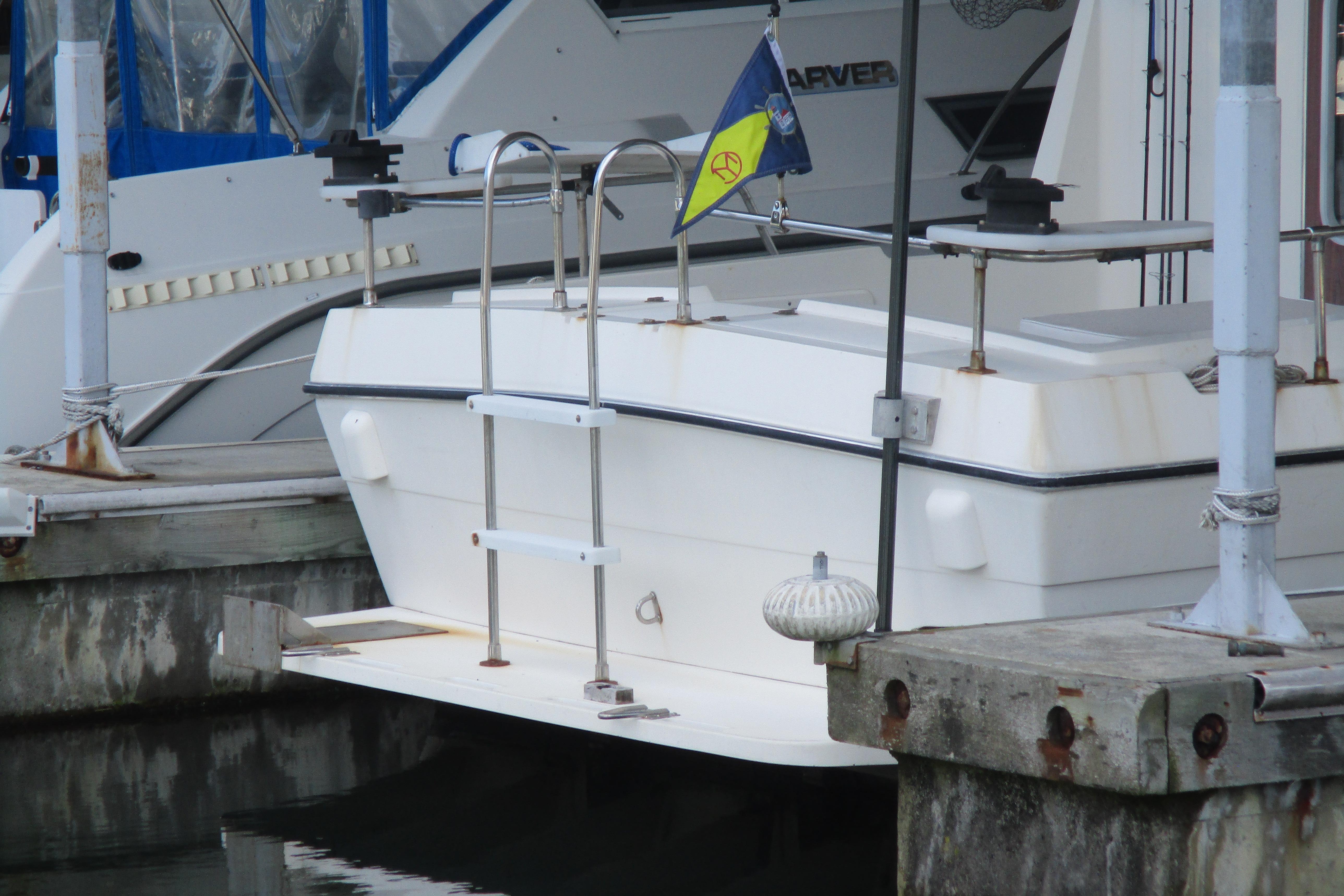1988 Commander 26 boat docked, featuring a ladder and a colorful flag at the stern.