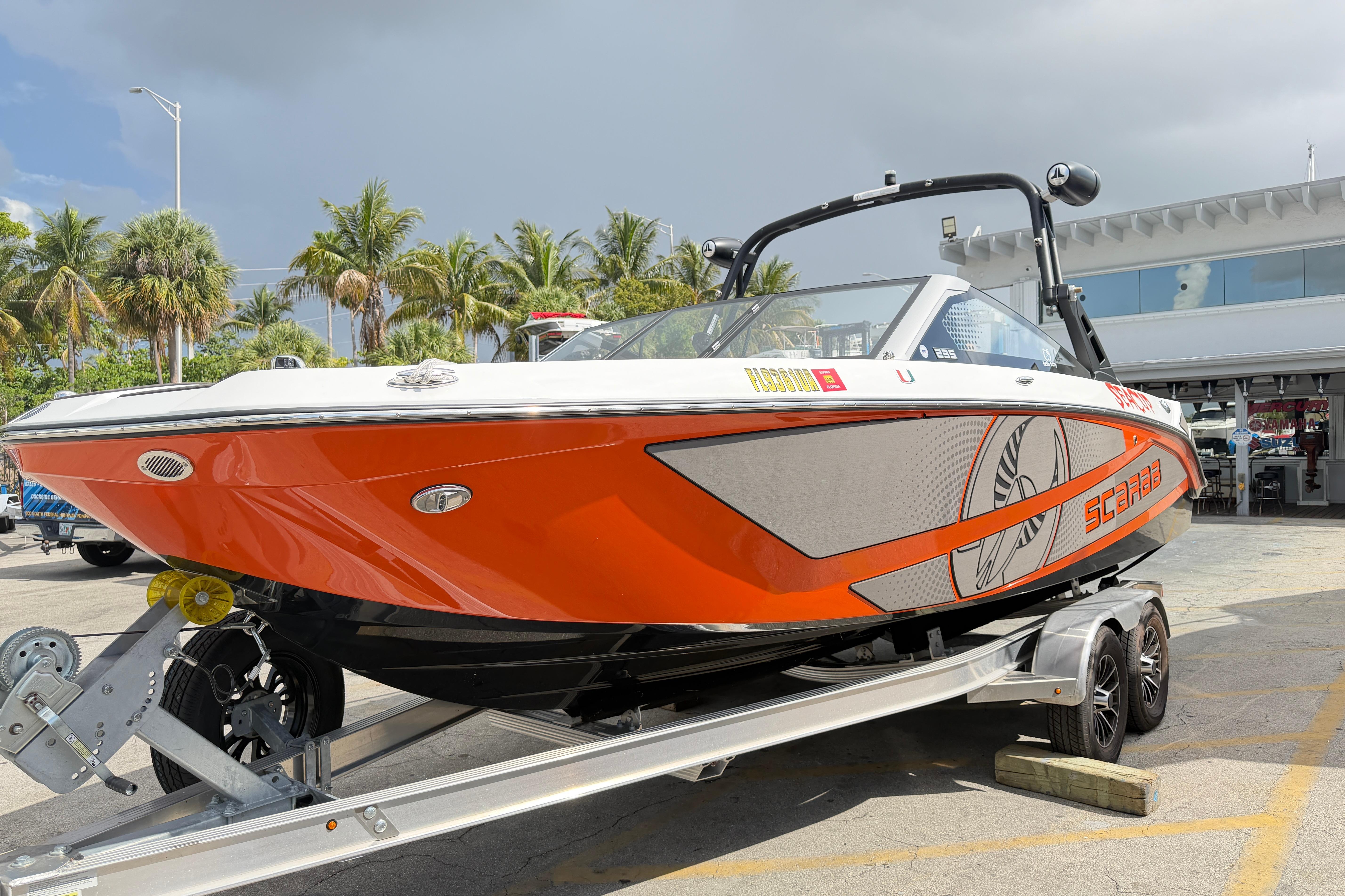 2026 Scarab 235 LX boat on trailer, vibrant orange design, parked near palm trees.