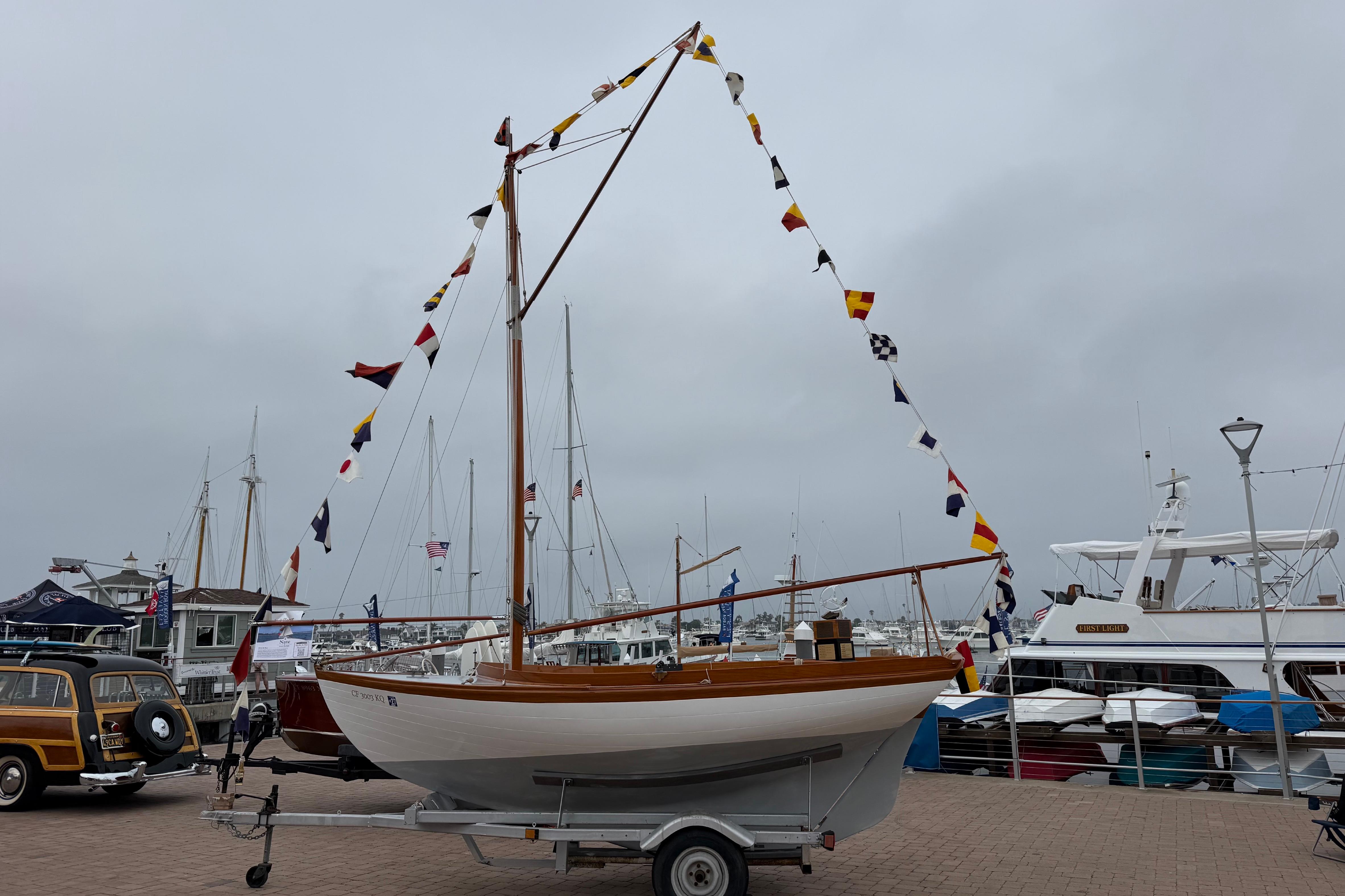 1920 Herreshoff 12.5 sailboat on trailer, adorned with colorful flags at marina.