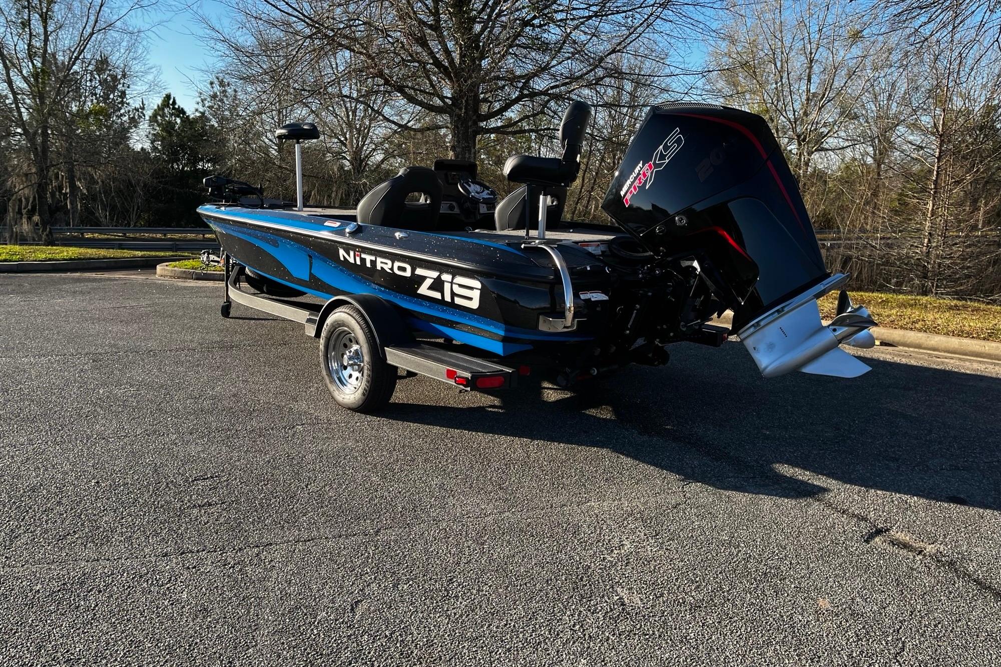 2024 Nitro Z19 boat with powerful engine, parked on asphalt, surrounded by trees.