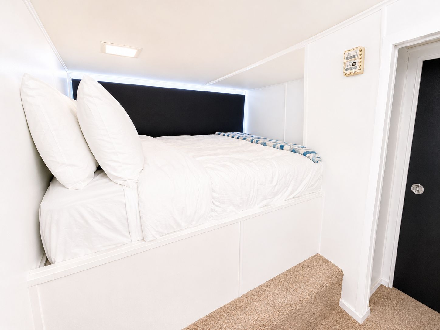 A cozy bedroom with a raised bed, white pillows, and a checkered blanket.
