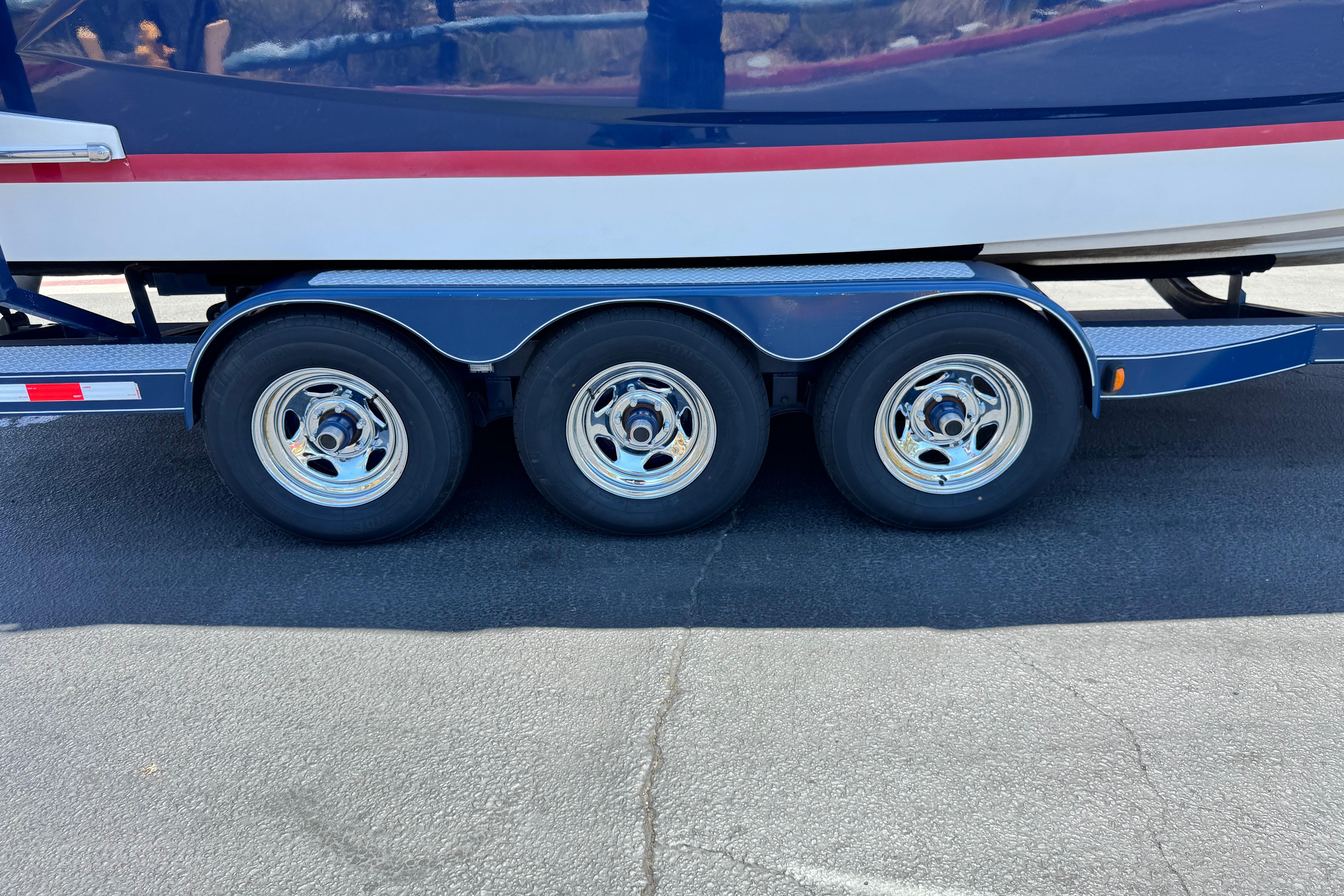 Trailer with triple-axle wheels for 2013 Regal 28 Express boat on pavement.
