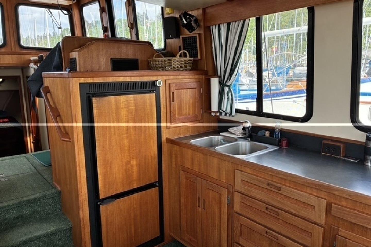 Interior of a 2000 Nordic Tug 37, featuring a wooden kitchen with sink and refrigerator.