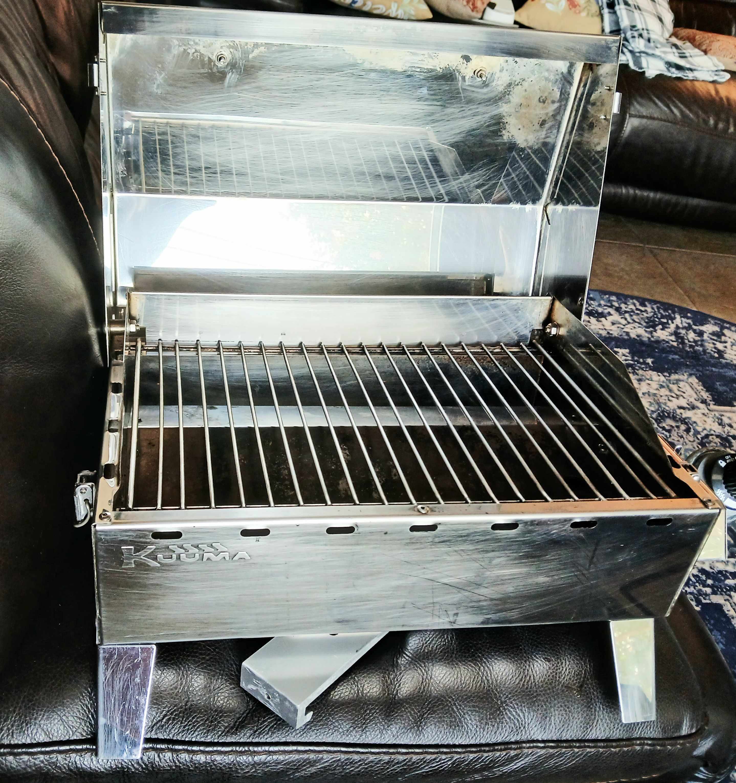 A stainless steel grill with an open lid on a leather sofa.