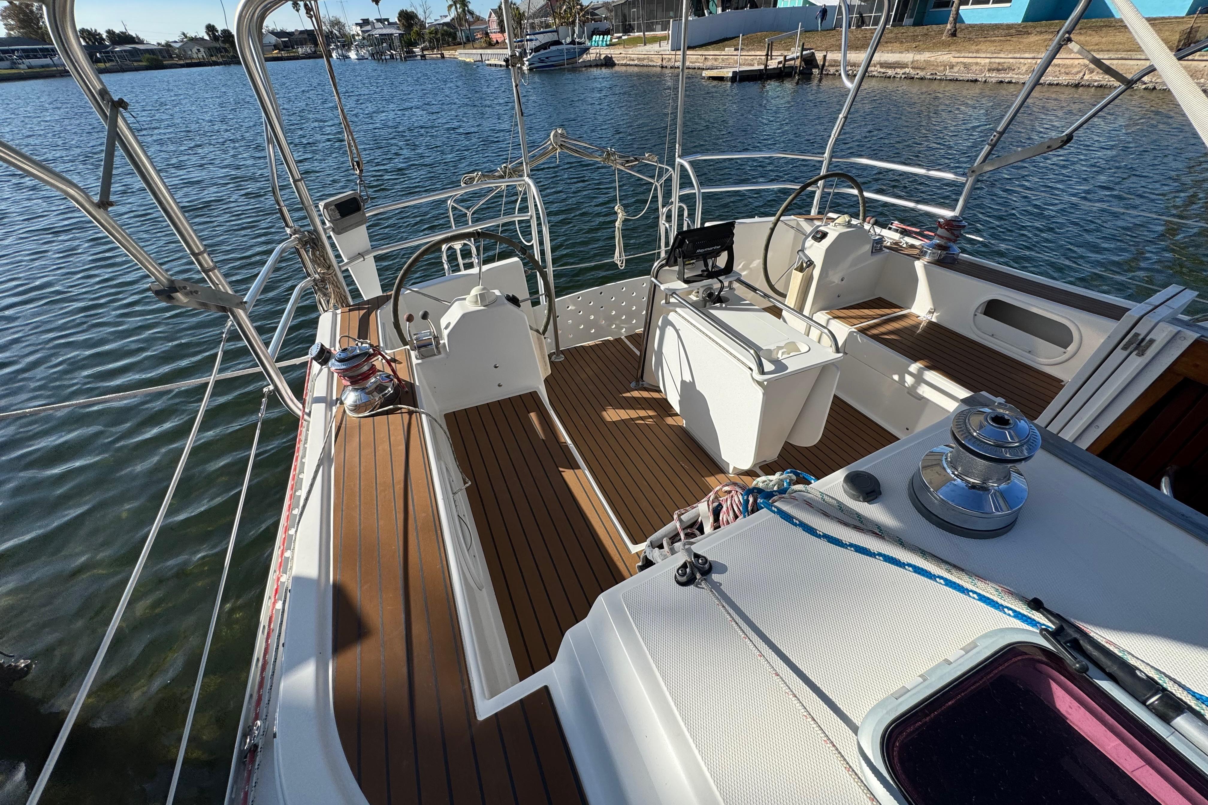 2006 Shannon Shoalsailer sailboat deck with wooden flooring and steering wheel, docked by the water.