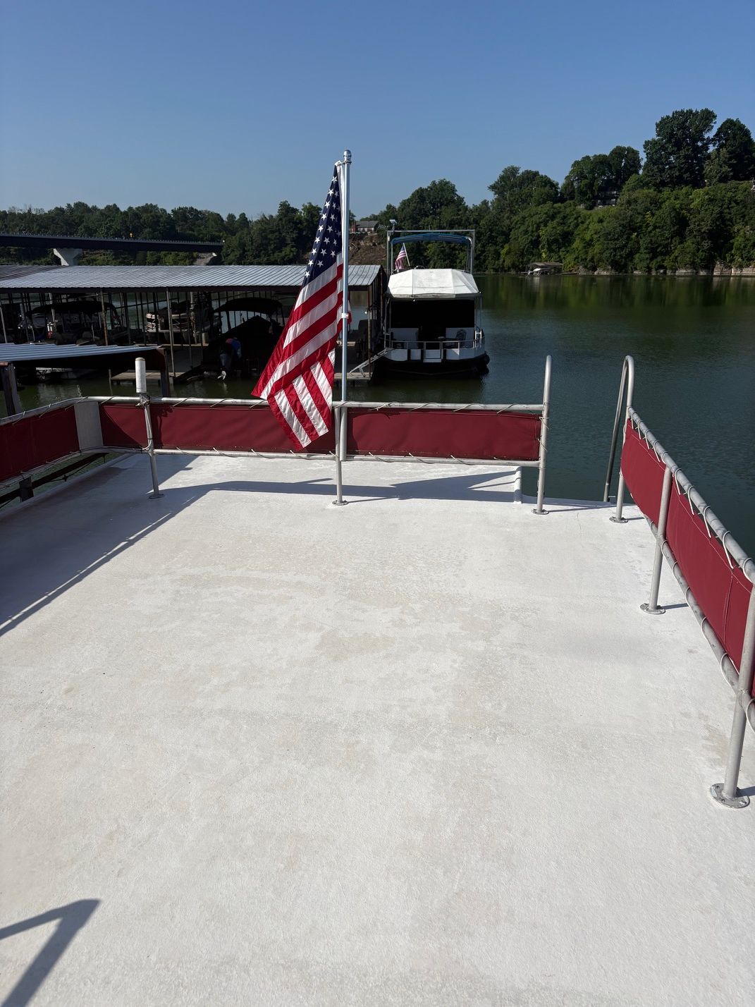 Top deck of a houseboat with railing and American flag, in a calm harbor.