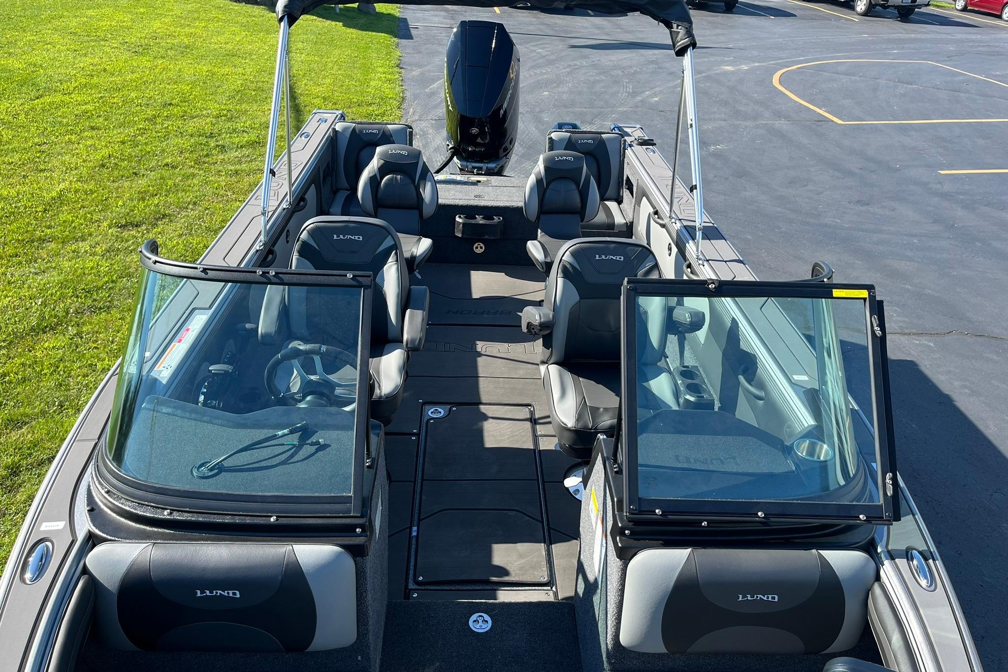 2026 Lund 2275 Baron boat interior with seating and windshield, parked on pavement.