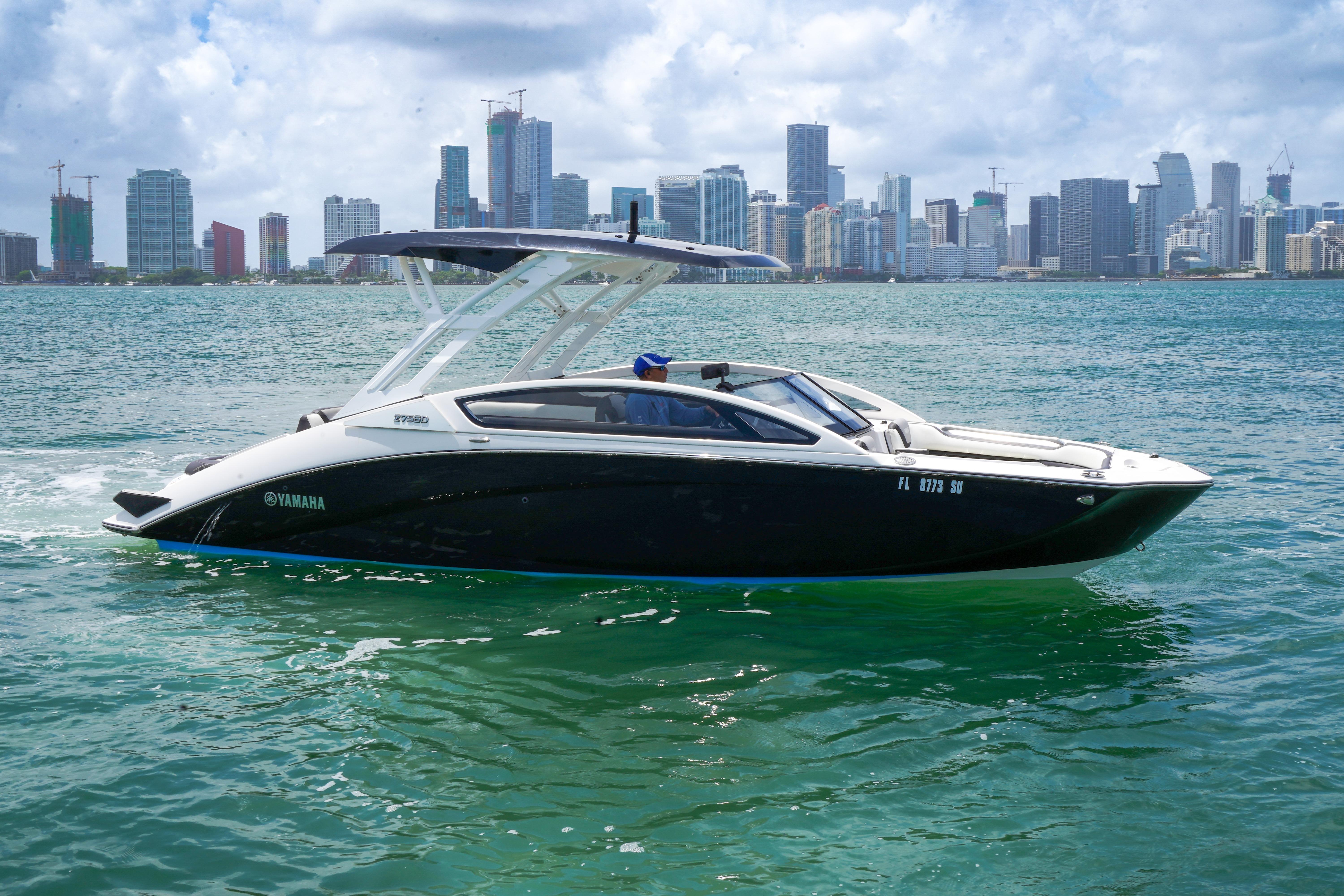 2021 Yamaha Boats 275SD cruising on water with city skyline backdrop.