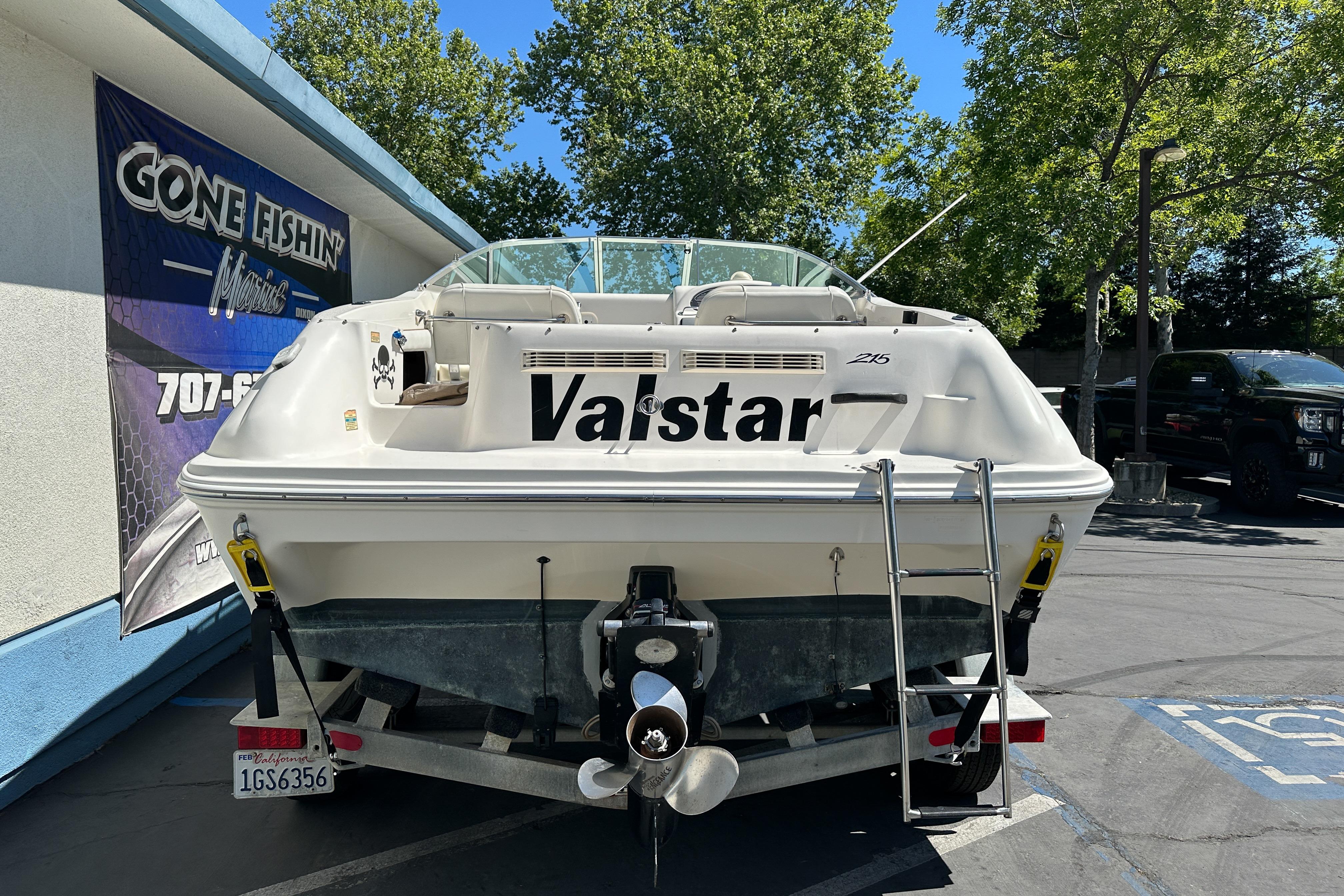 1998 Sea Ray 215 Express Cruiser on trailer, parked outdoors near "Gone Fishin'" sign.