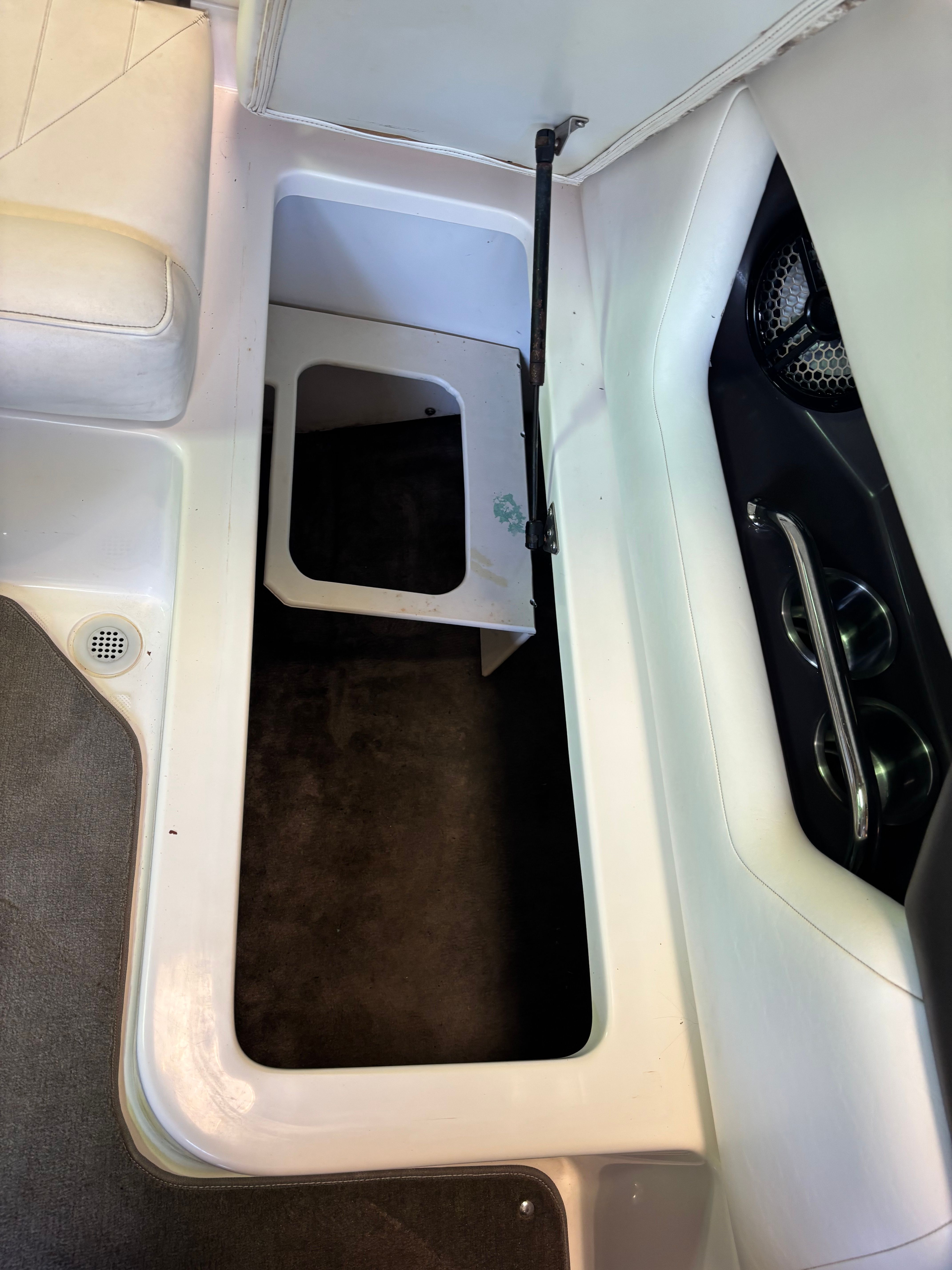 An open storage compartment inside a boat with white upholstery and carpeted flooring.