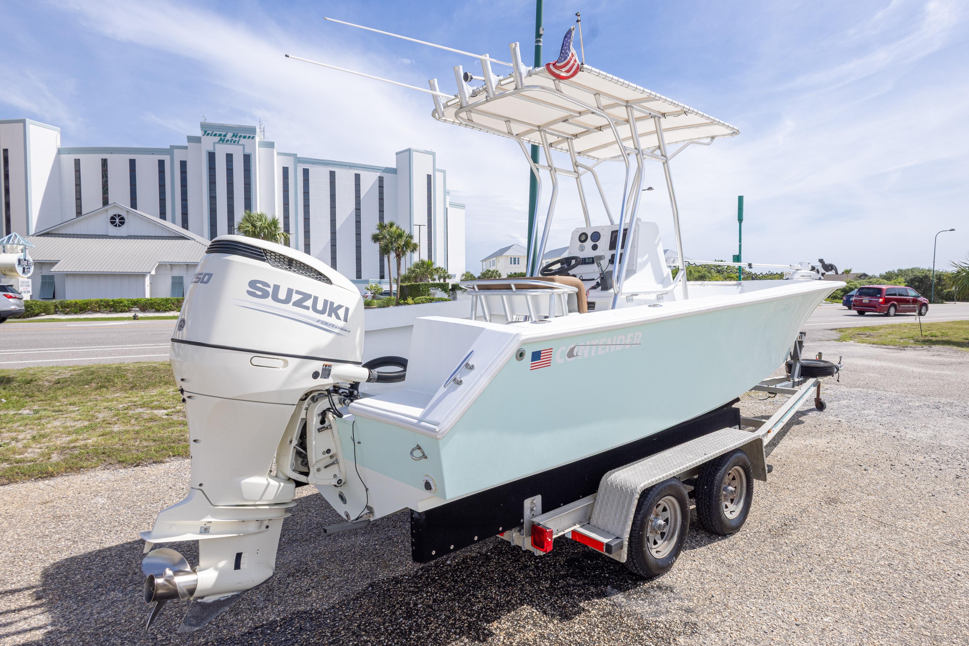 1998 Contender 21 CC boat on trailer with Suzuki engine, parked near a hotel.