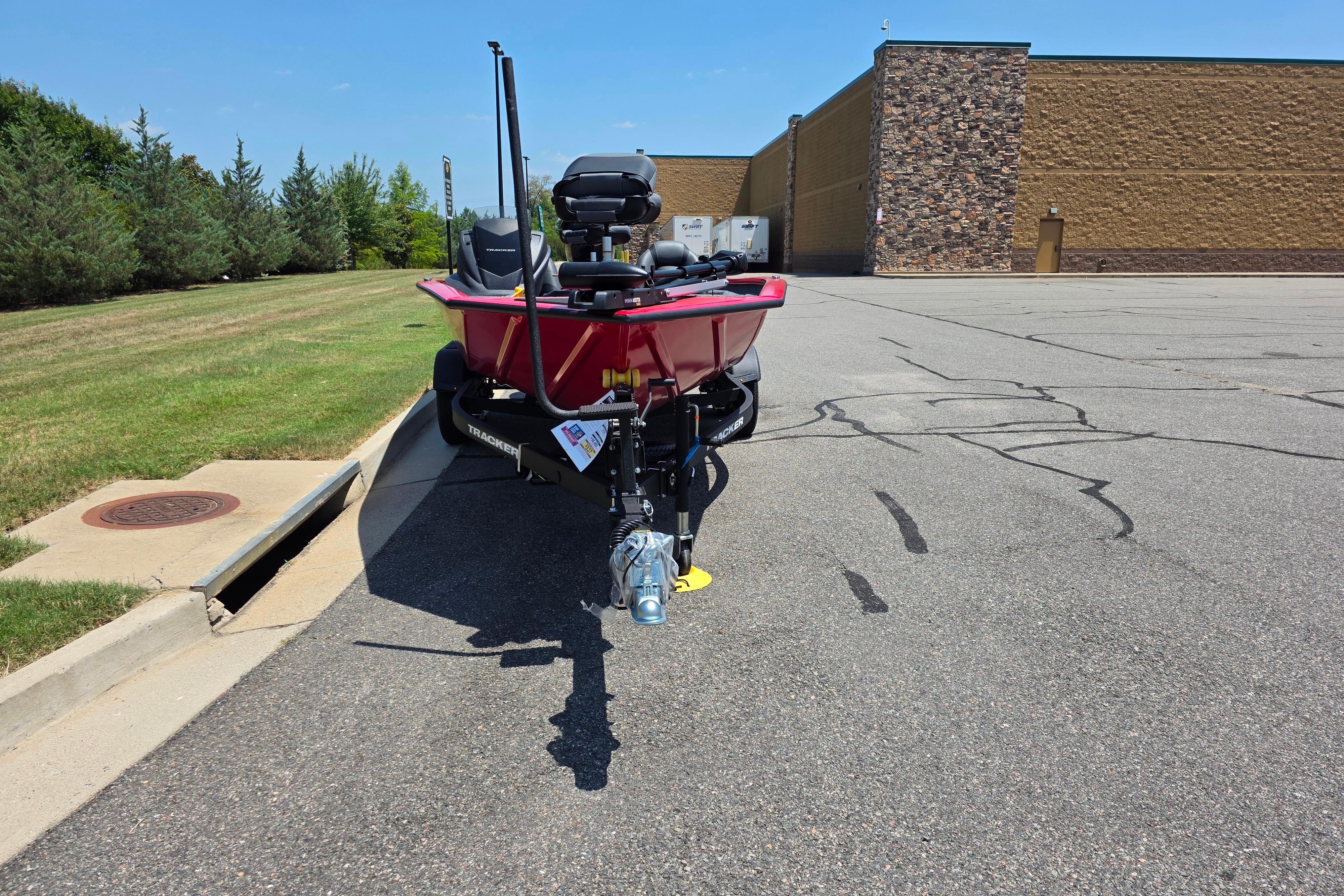 2026 Tracker Pro Team 195 boat parked on asphalt near a grassy area and building.
