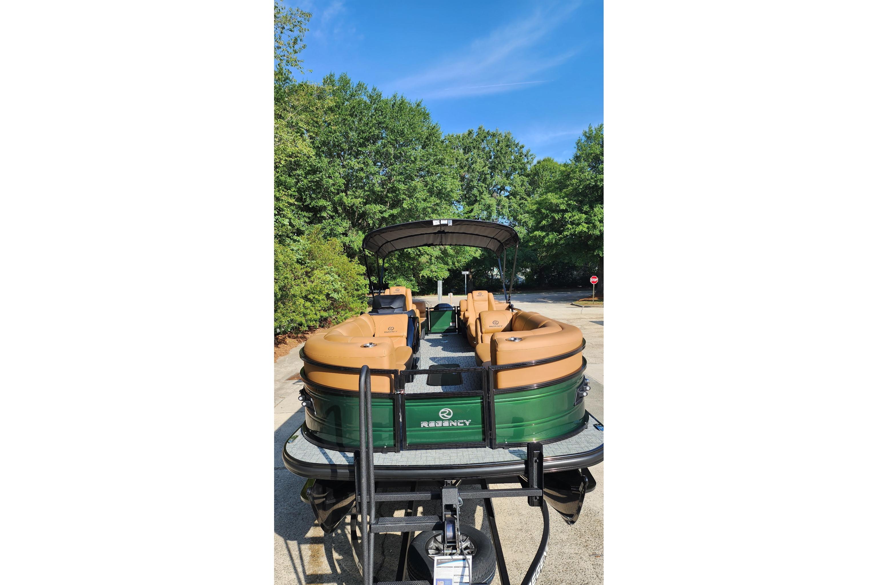 2026 Regency 230 DL pontoon boat on trailer, surrounded by lush greenery.