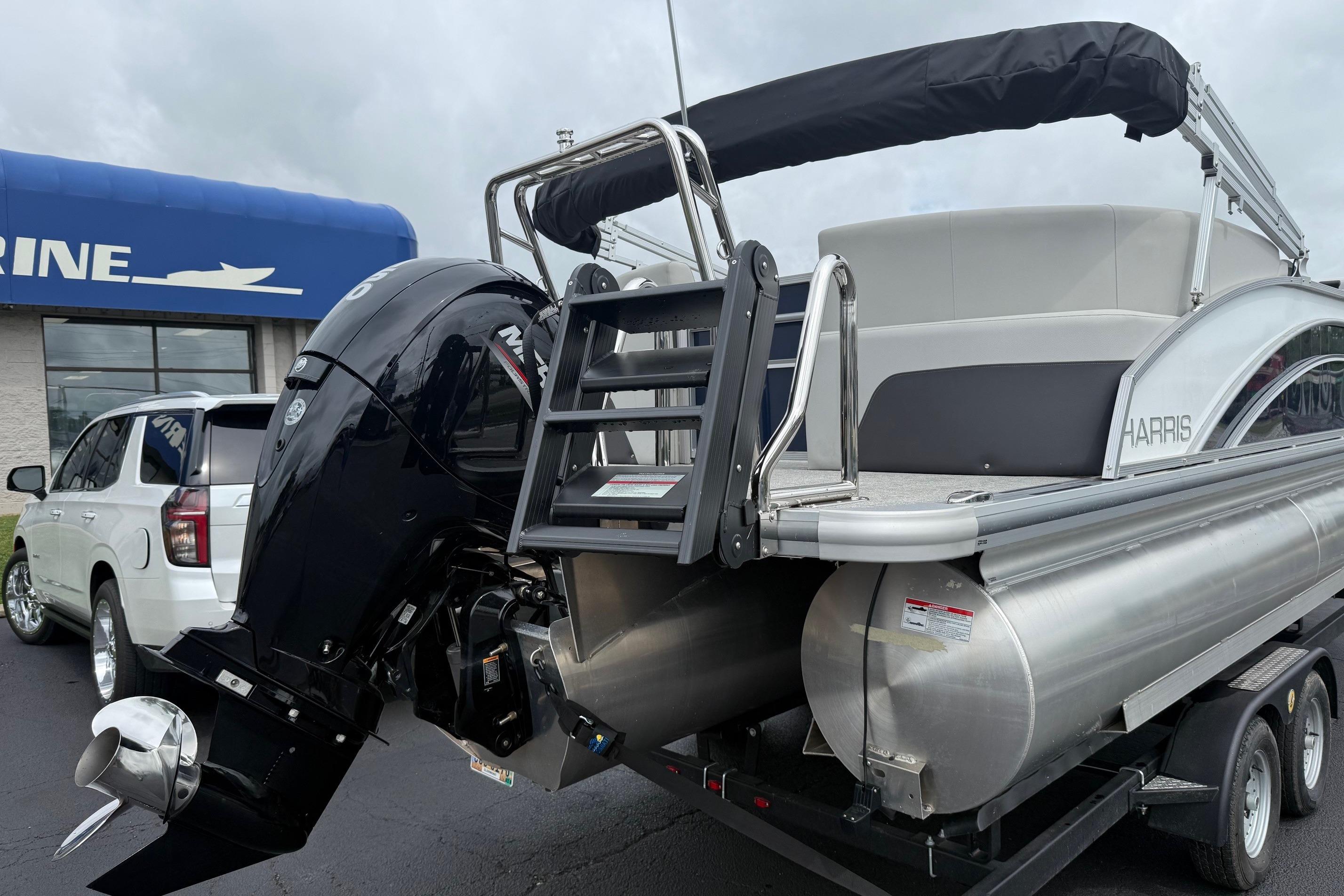 2025 Harris Cruiser 230 pontoon boat with outboard motor, parked near a marine dealership.
