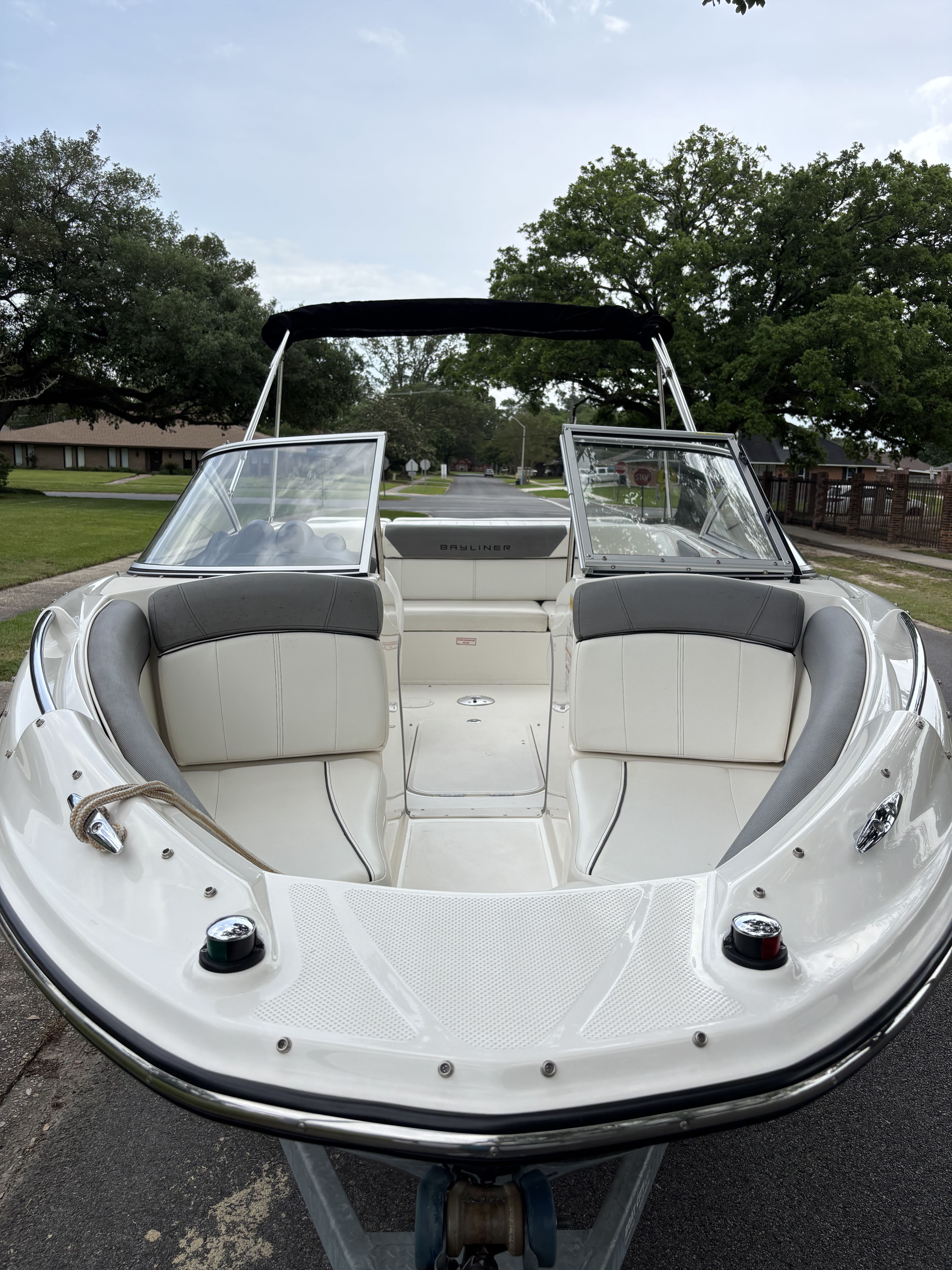 A Bayliner 215 Bowrider boat on a trailer, surrounded by trees and houses.