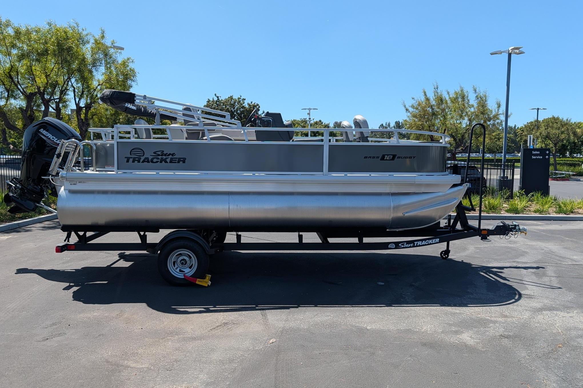 2026 Sun Tracker Bass Buggy 18 DLX pontoon boat on trailer in parking lot.