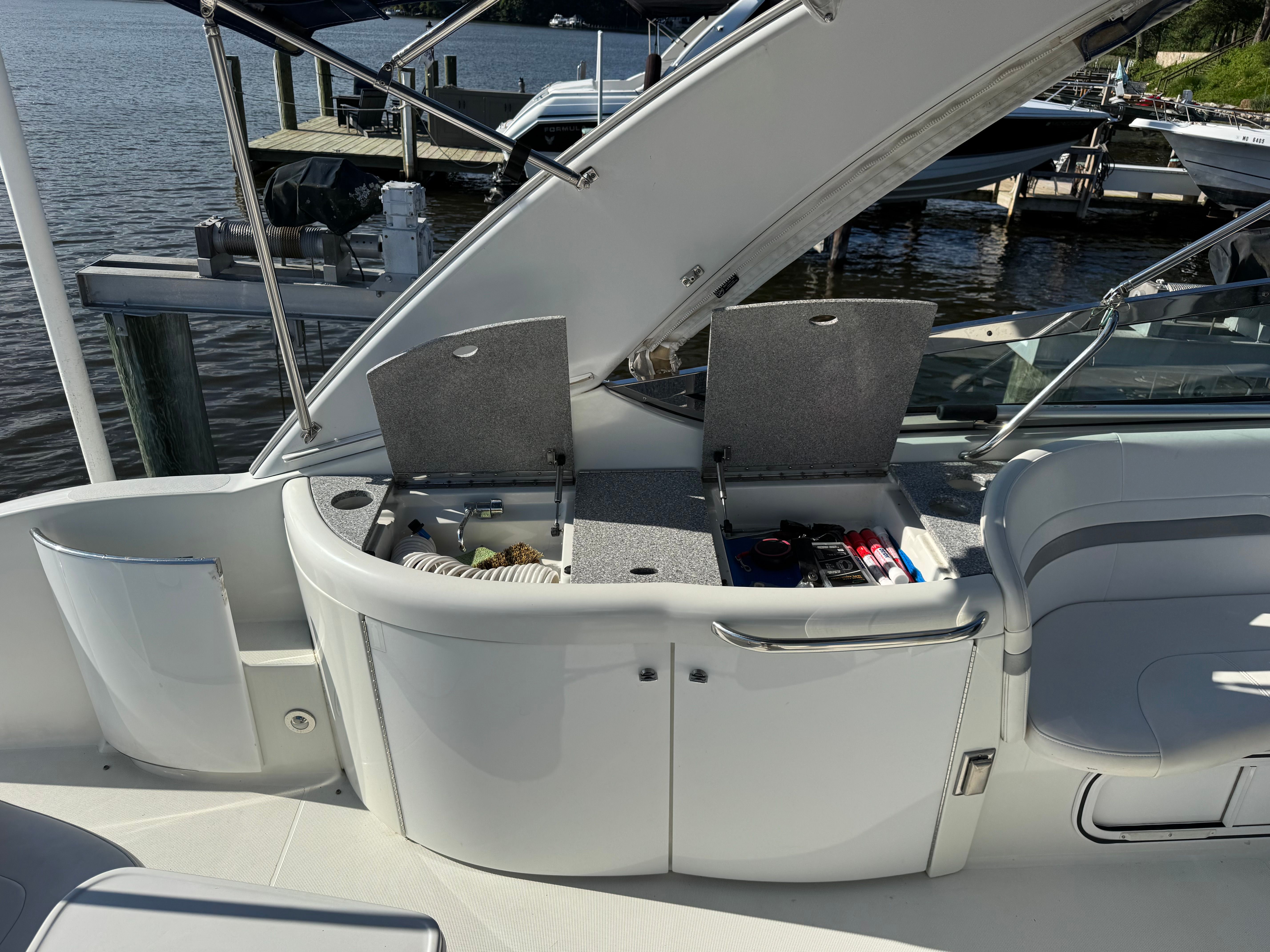 The boat has an open storage compartment with accessories, docked by the water.