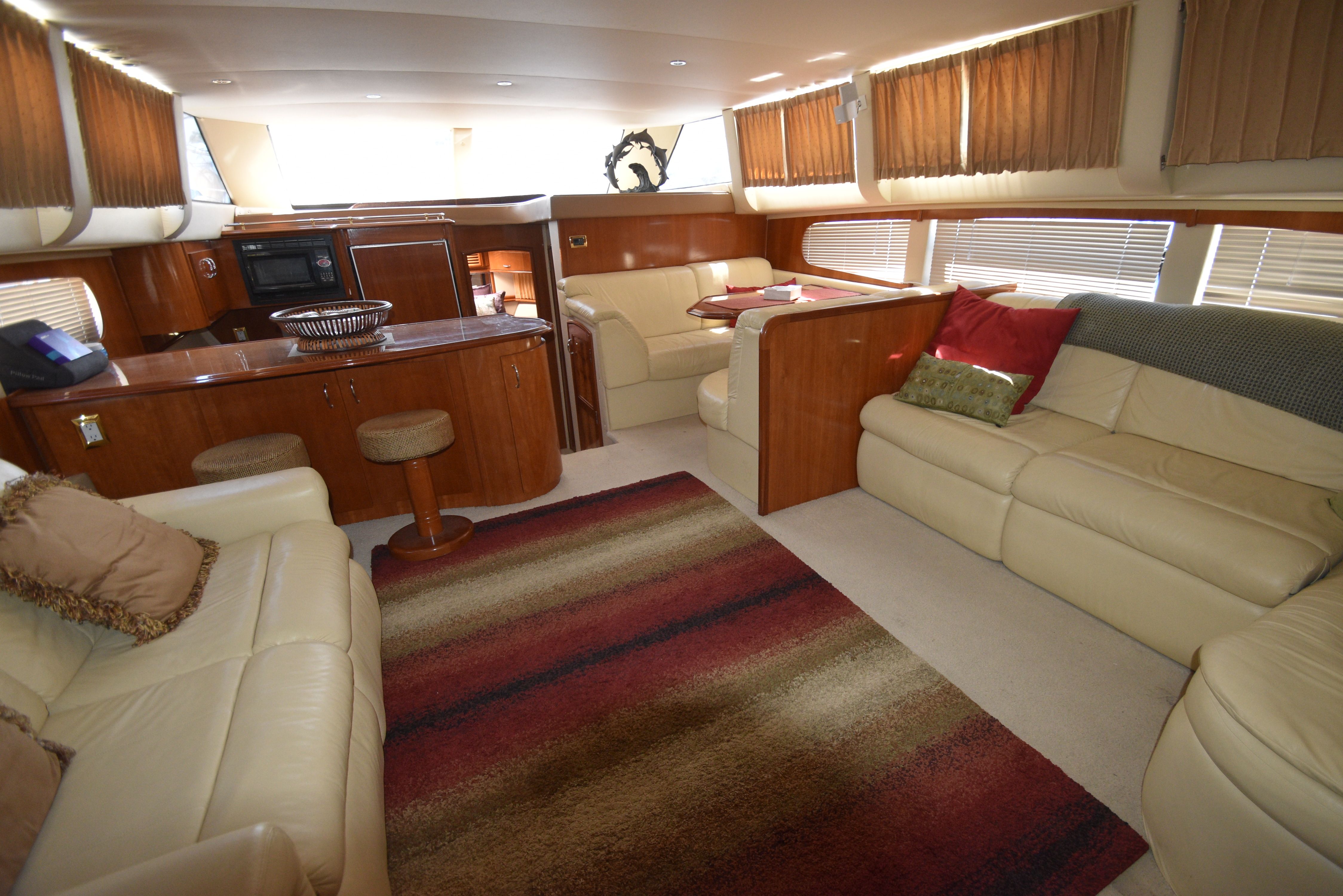 Interior of a luxurious yacht with beige leather sofas, carpet, and kitchen area.