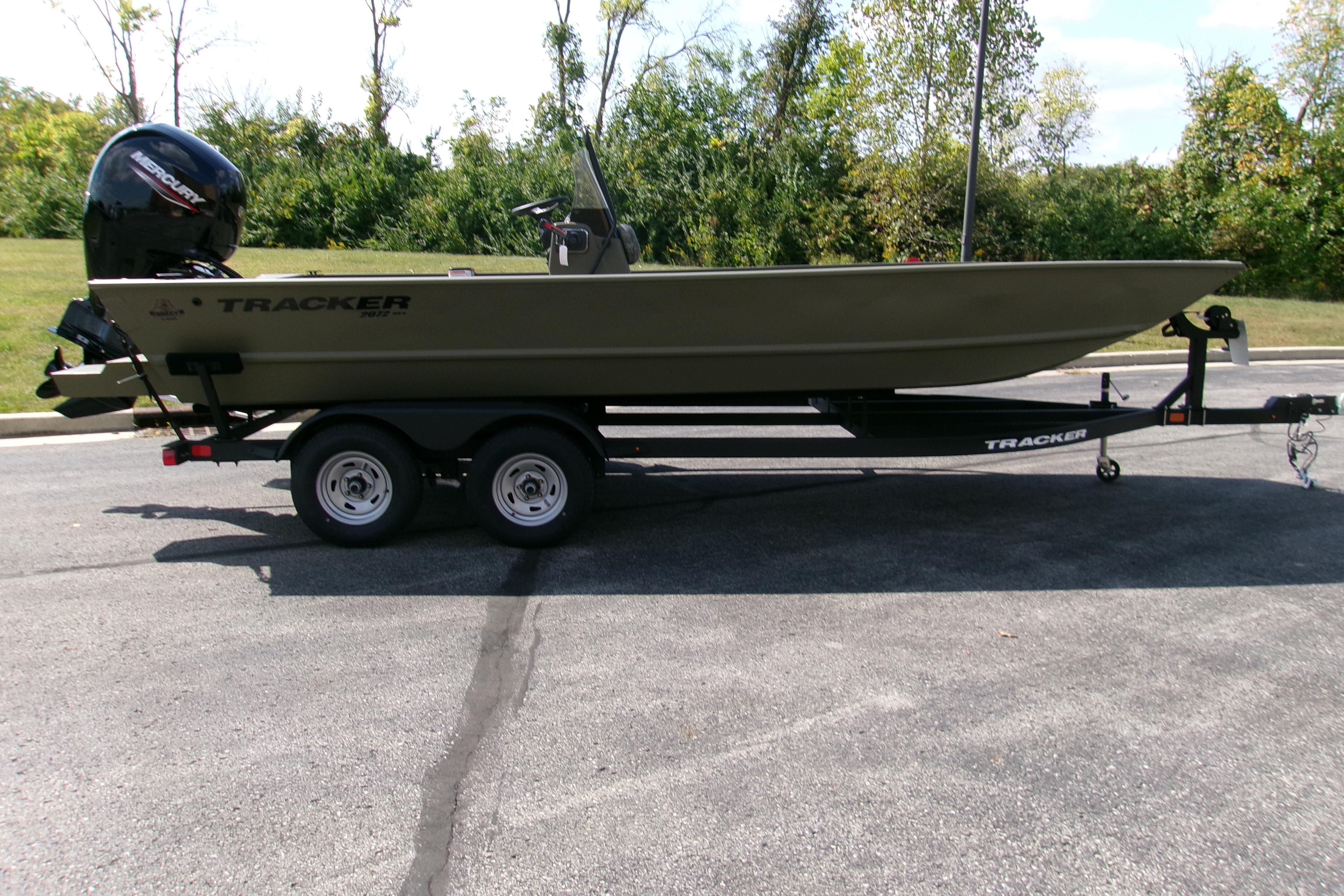 2026 Tracker Grizzly 2072 CC boat on trailer, parked on asphalt, surrounded by greenery.