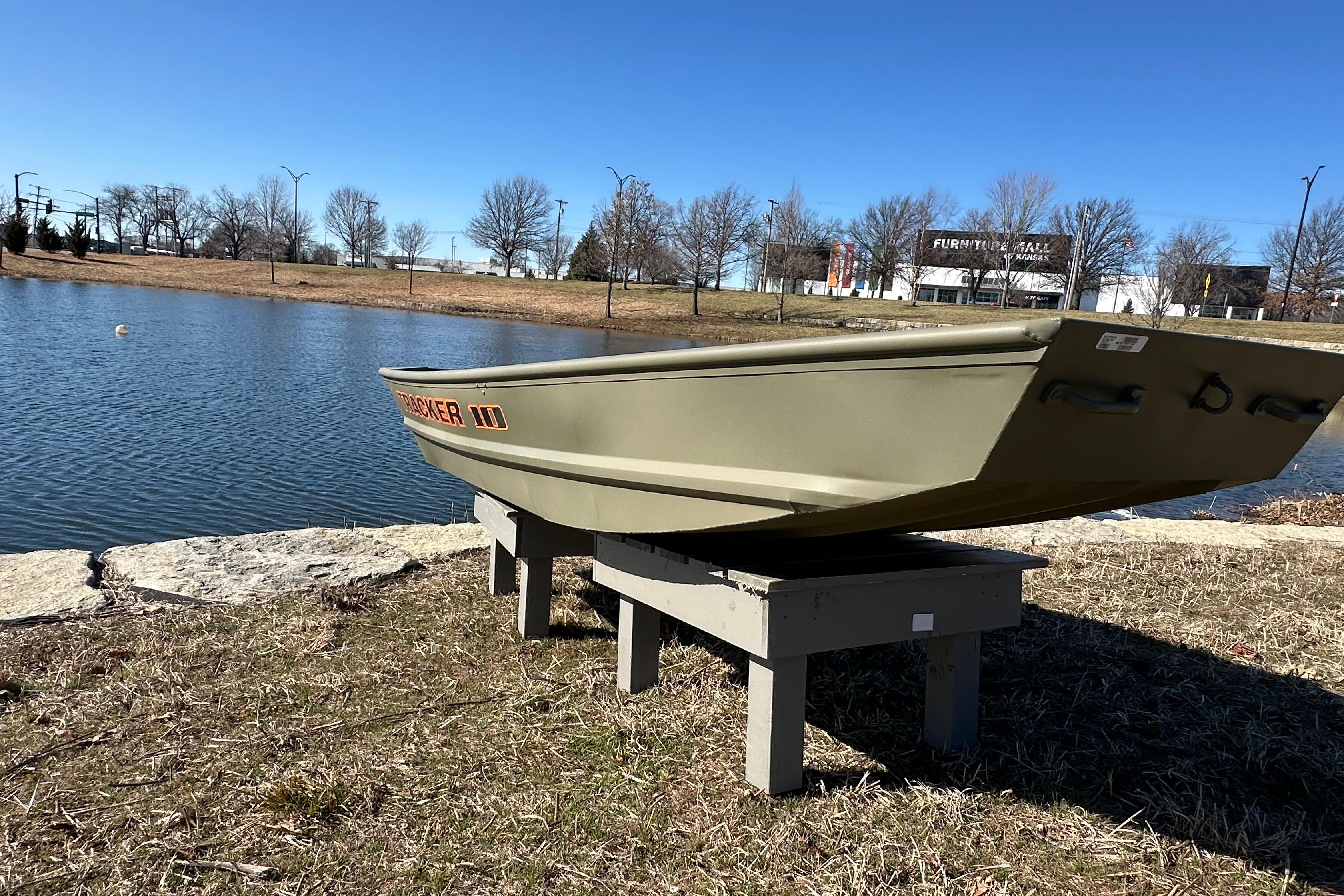 2026 Tracker Grizzly 10 Jon boat displayed by a serene lake under clear blue skies.