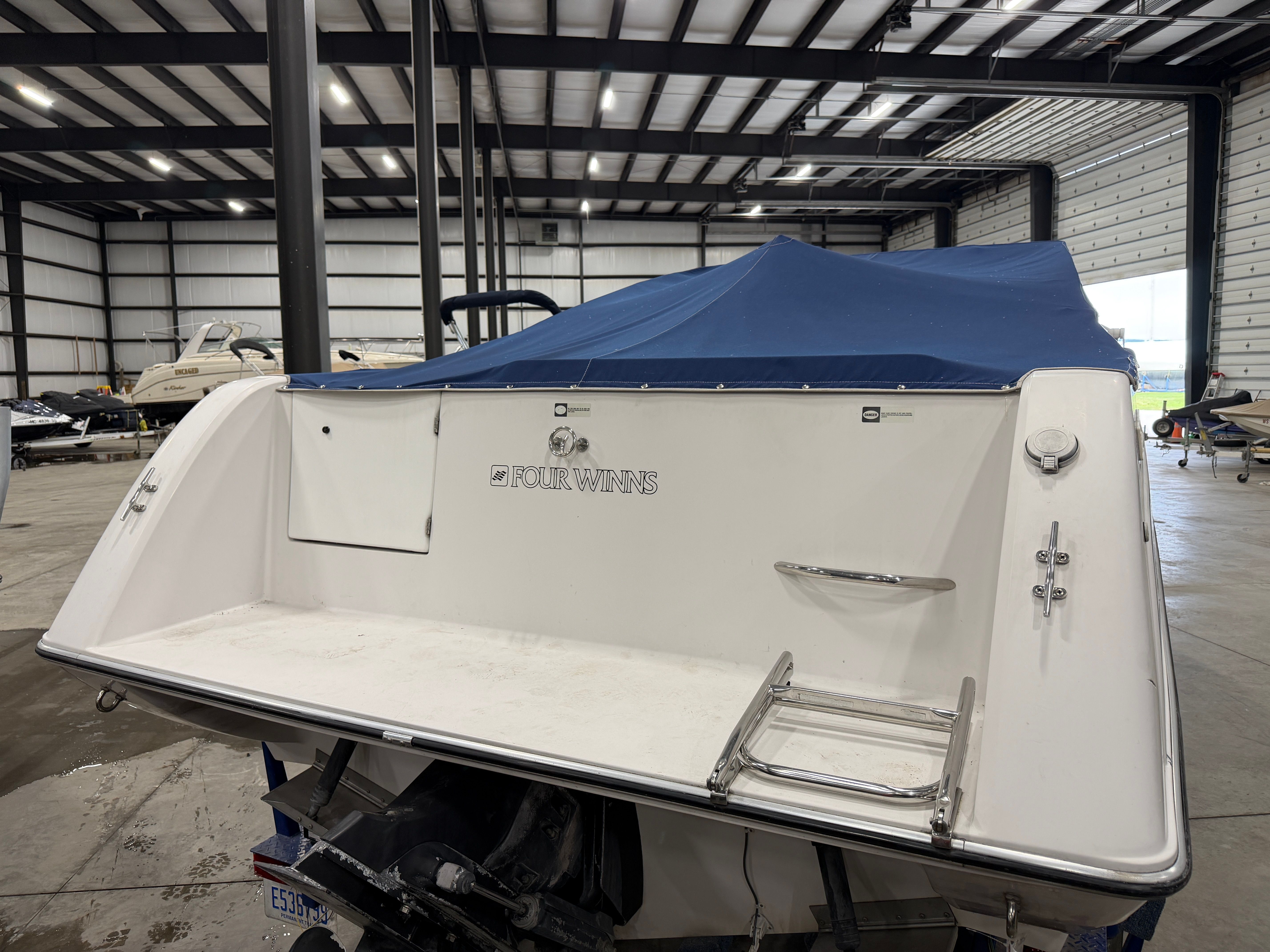 The image shows the stern of a 1992 Four Winns 225 Sundowner with a blue cover in a storage facility.