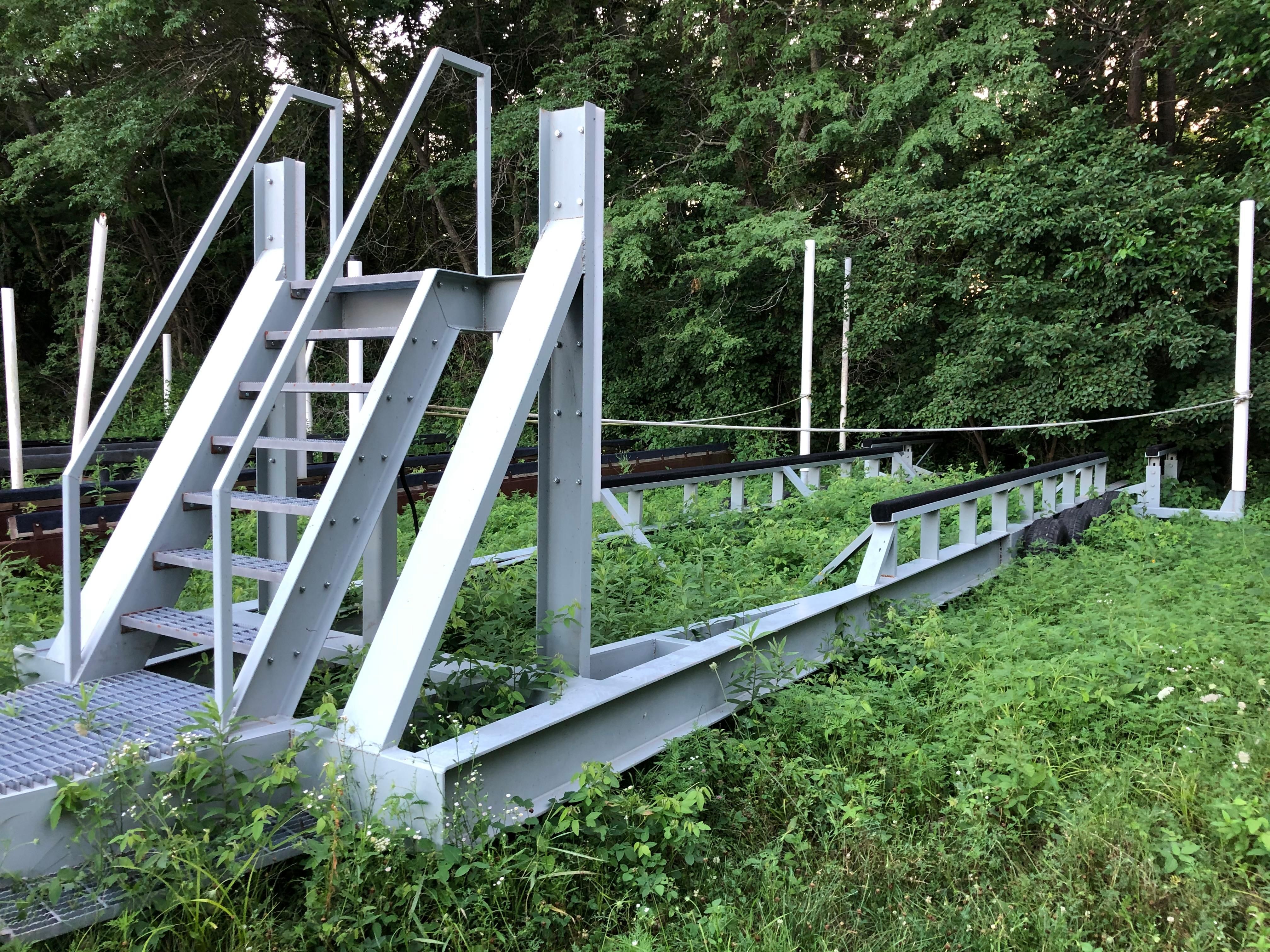 A metal boat lift sits on grassy terrain with trees in the background.