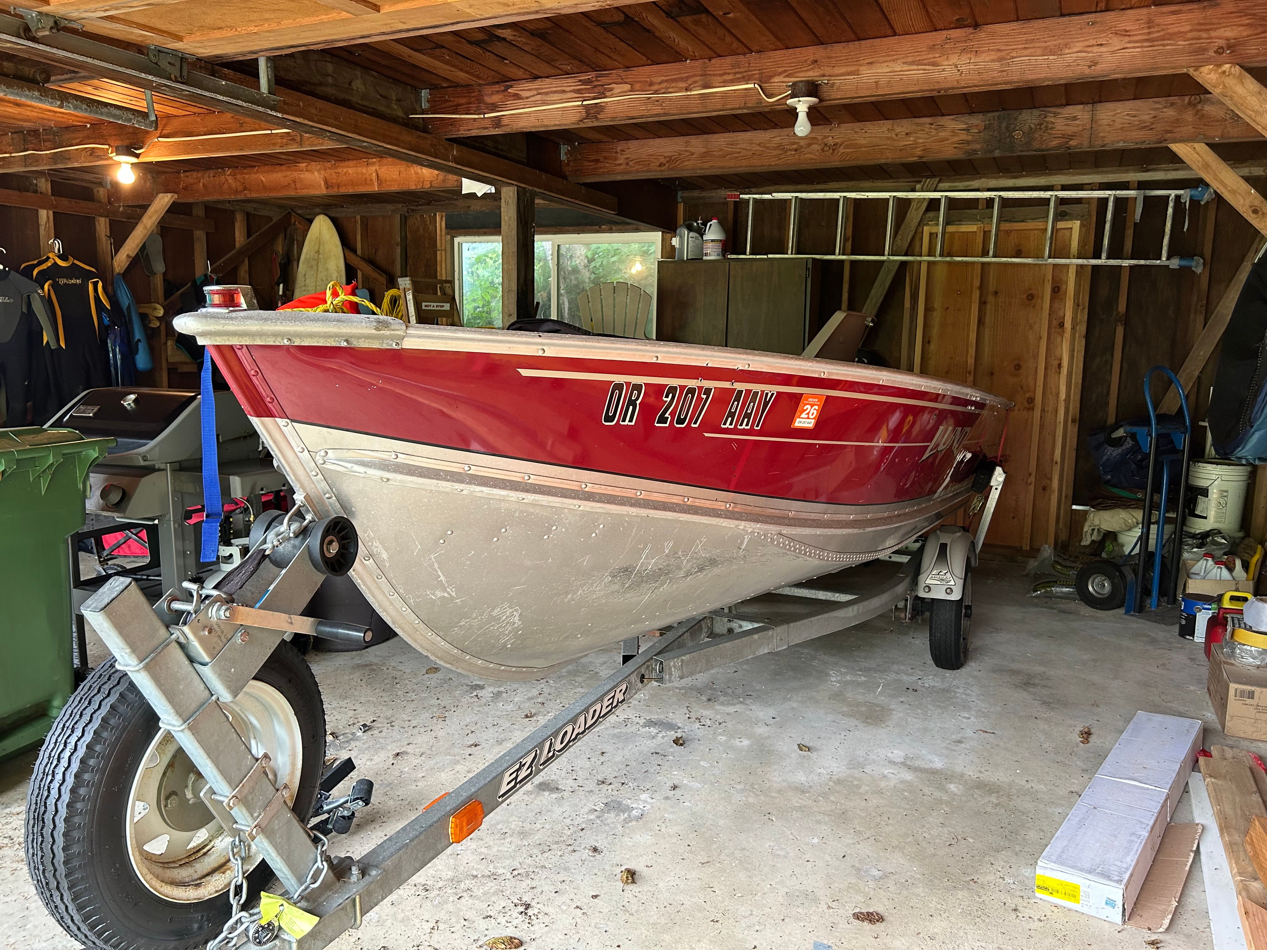 A red 2002 Lund boat is on a trailer in a garage.