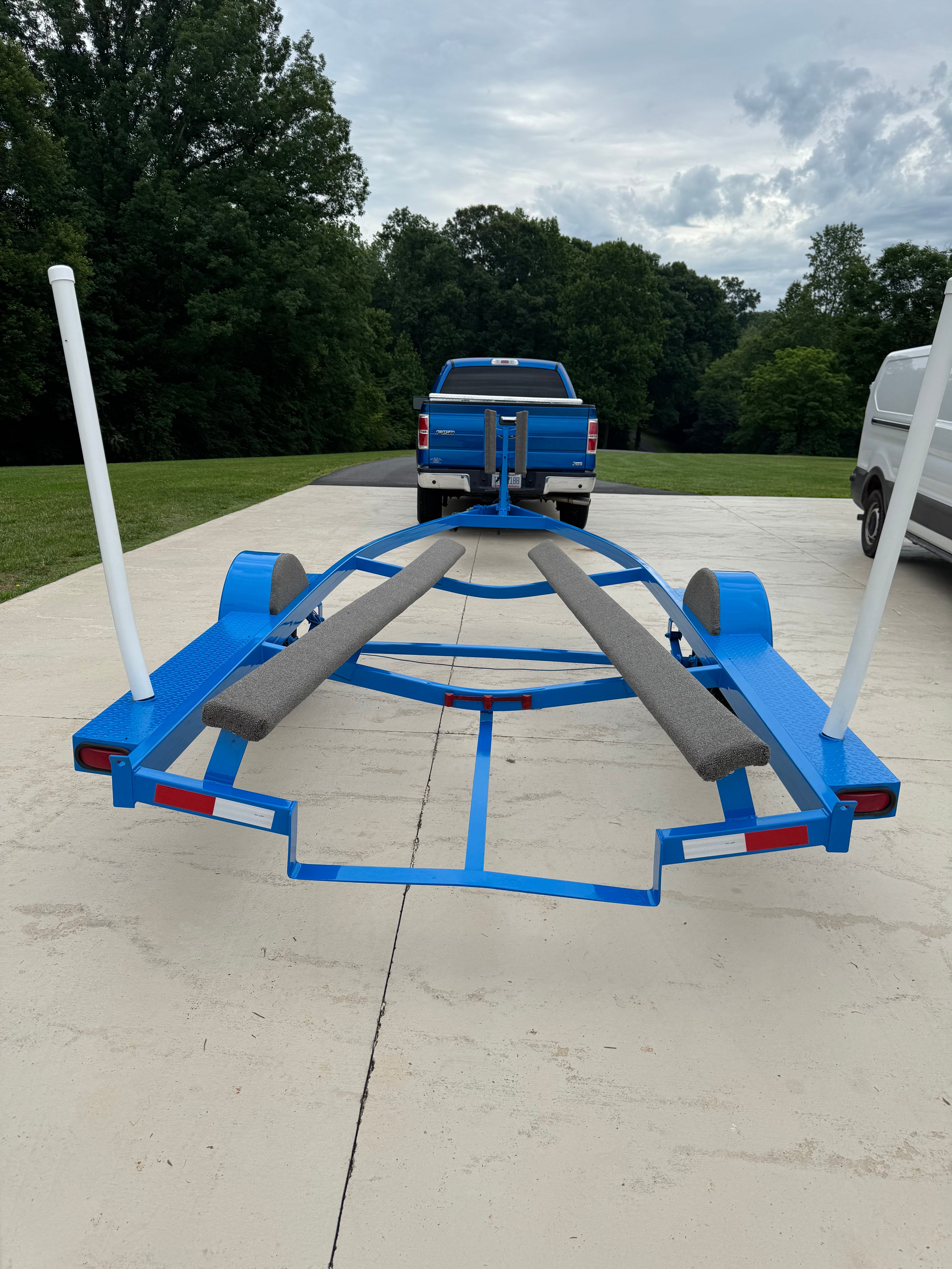 Blue boat trailer on driveway, surrounded by trees.