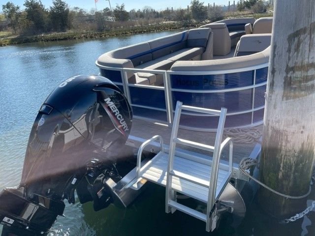 A 2023 Bennington pontoon boat is docked. It features a Mercury outboard motor.