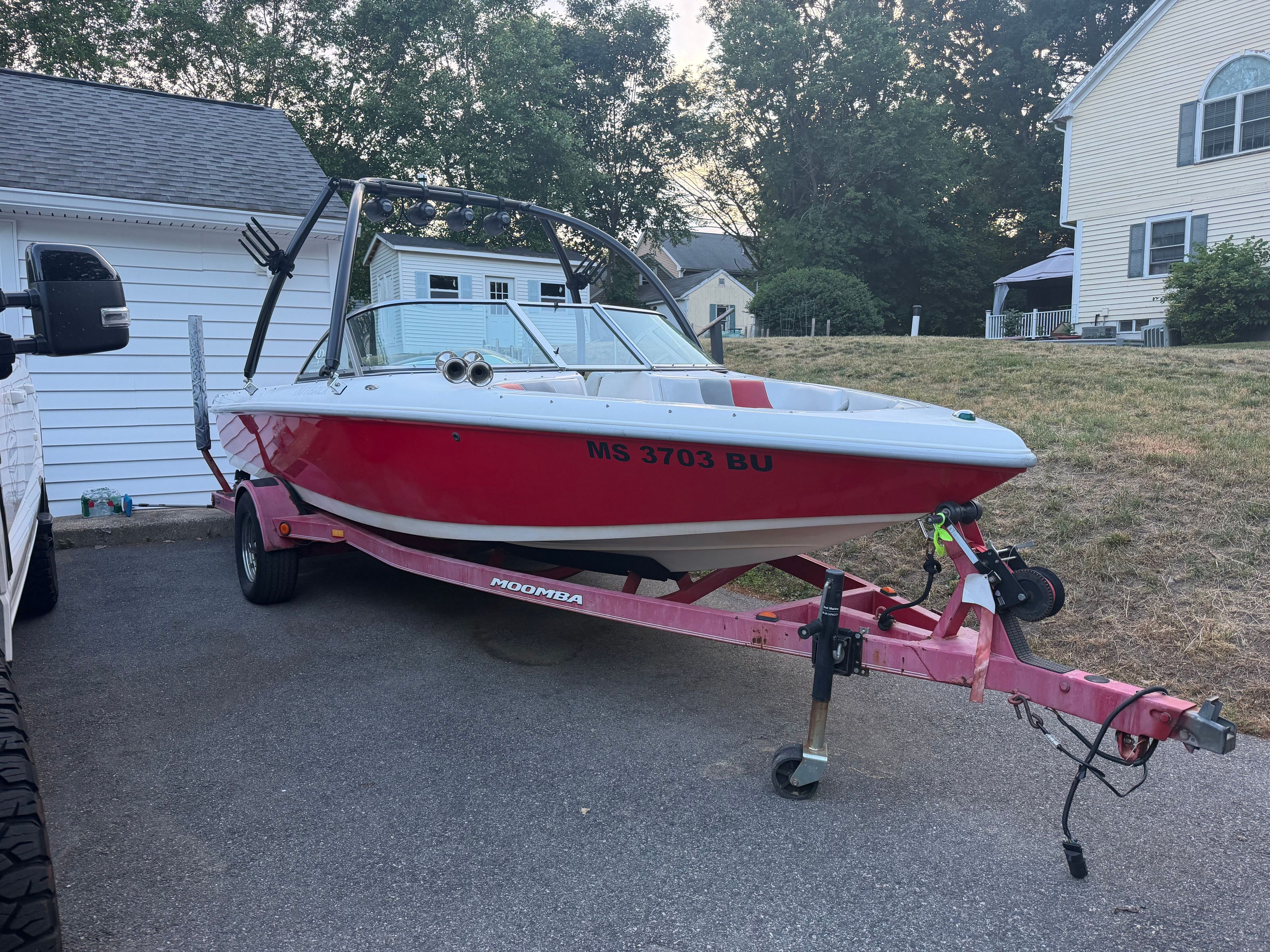 A red 2002 Moomba Outback boat is on a trailer in a driveway.