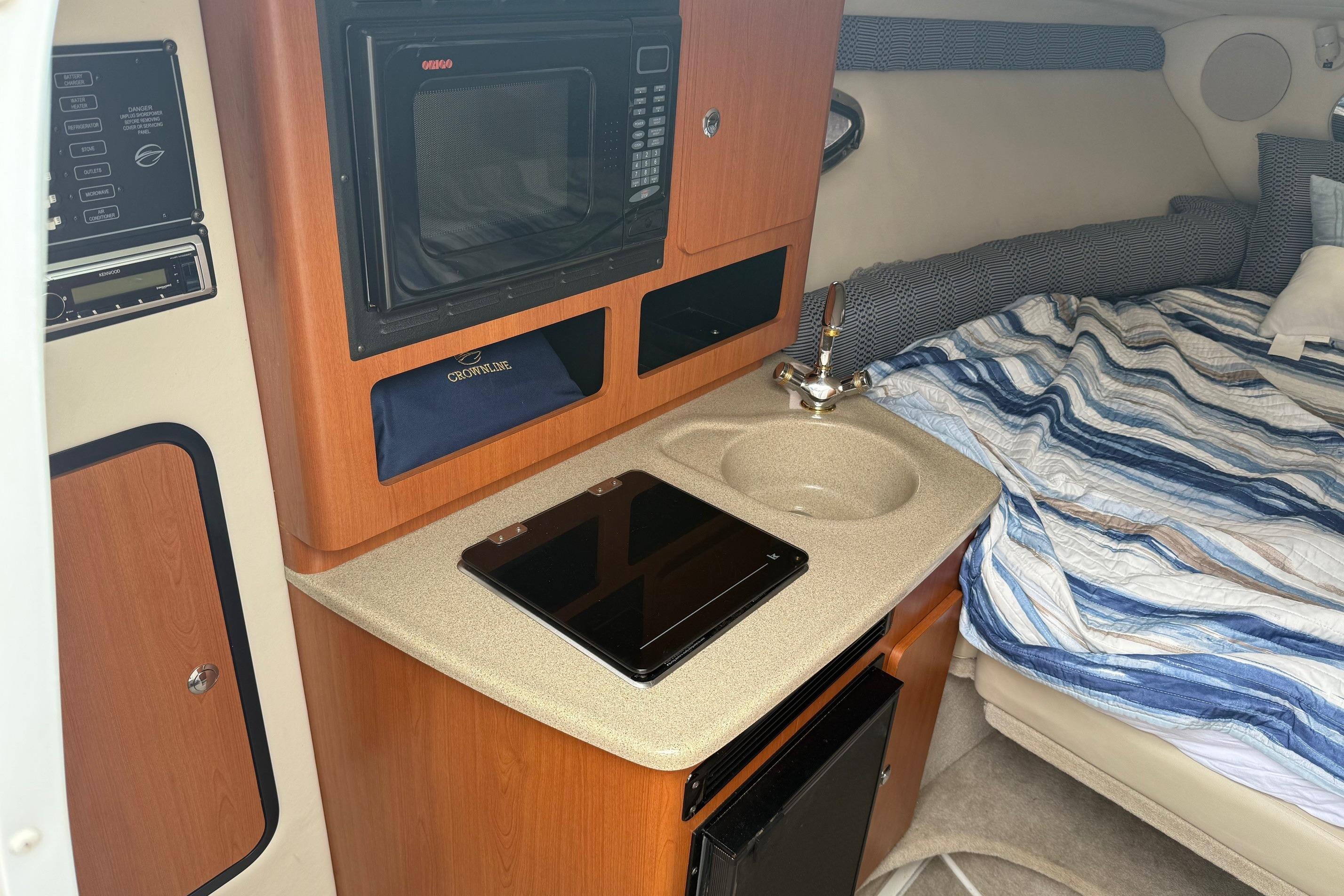 2005 Crownline 250 CR cabin with kitchenette, microwave, sink, and cozy bed.
