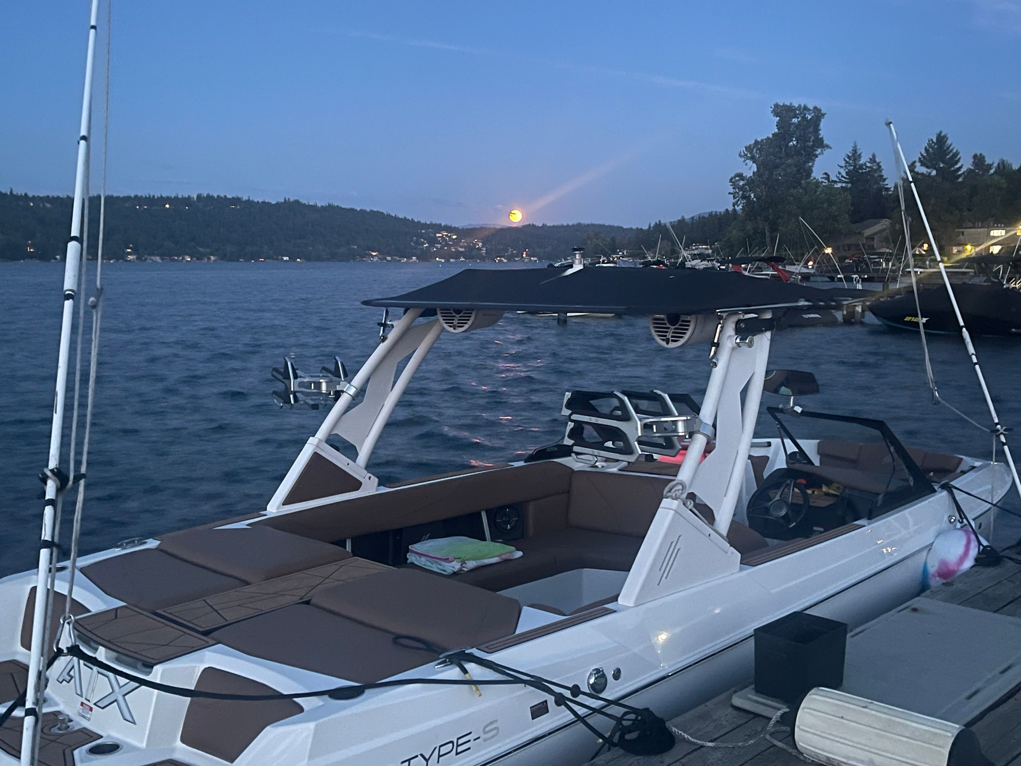 A 2022 ATX Surf Boat 22 Type-S docked at sunset with a scenic backdrop.