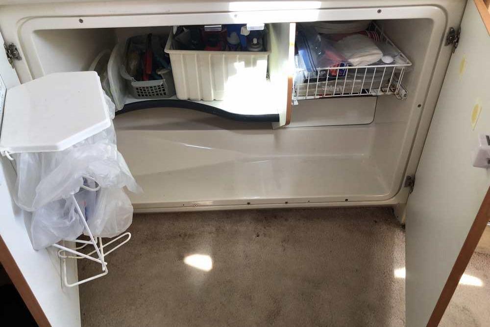 Cabinet storage inside a 1999 Regal Commodore 2760 boat, featuring organized shelves and a trash bag holder.