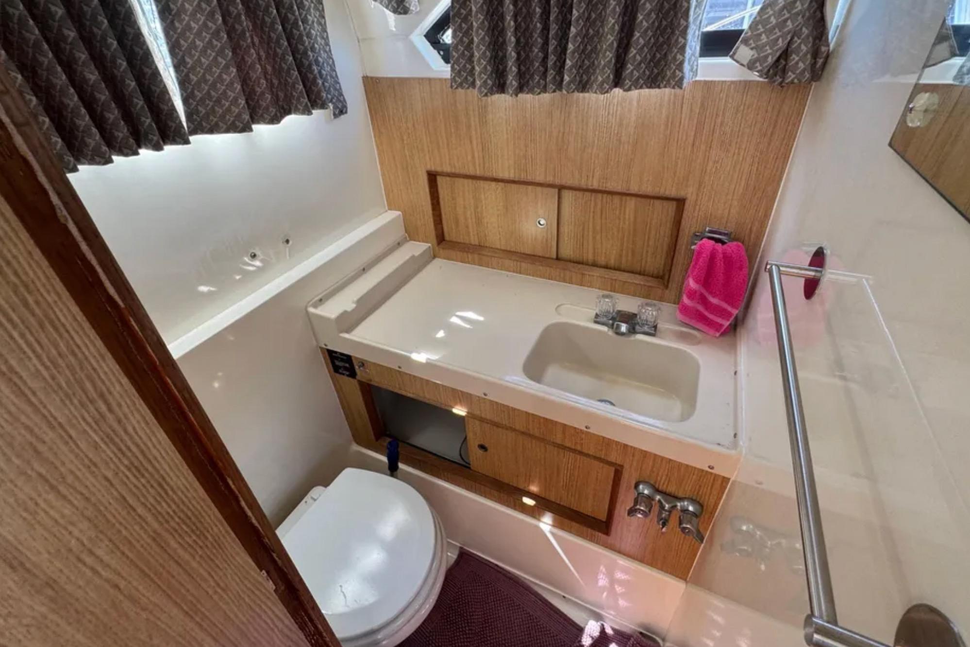 Bathroom interior of 1988 Bertram 28 Sport Fisherman, featuring sink, toilet, and wooden cabinetry.