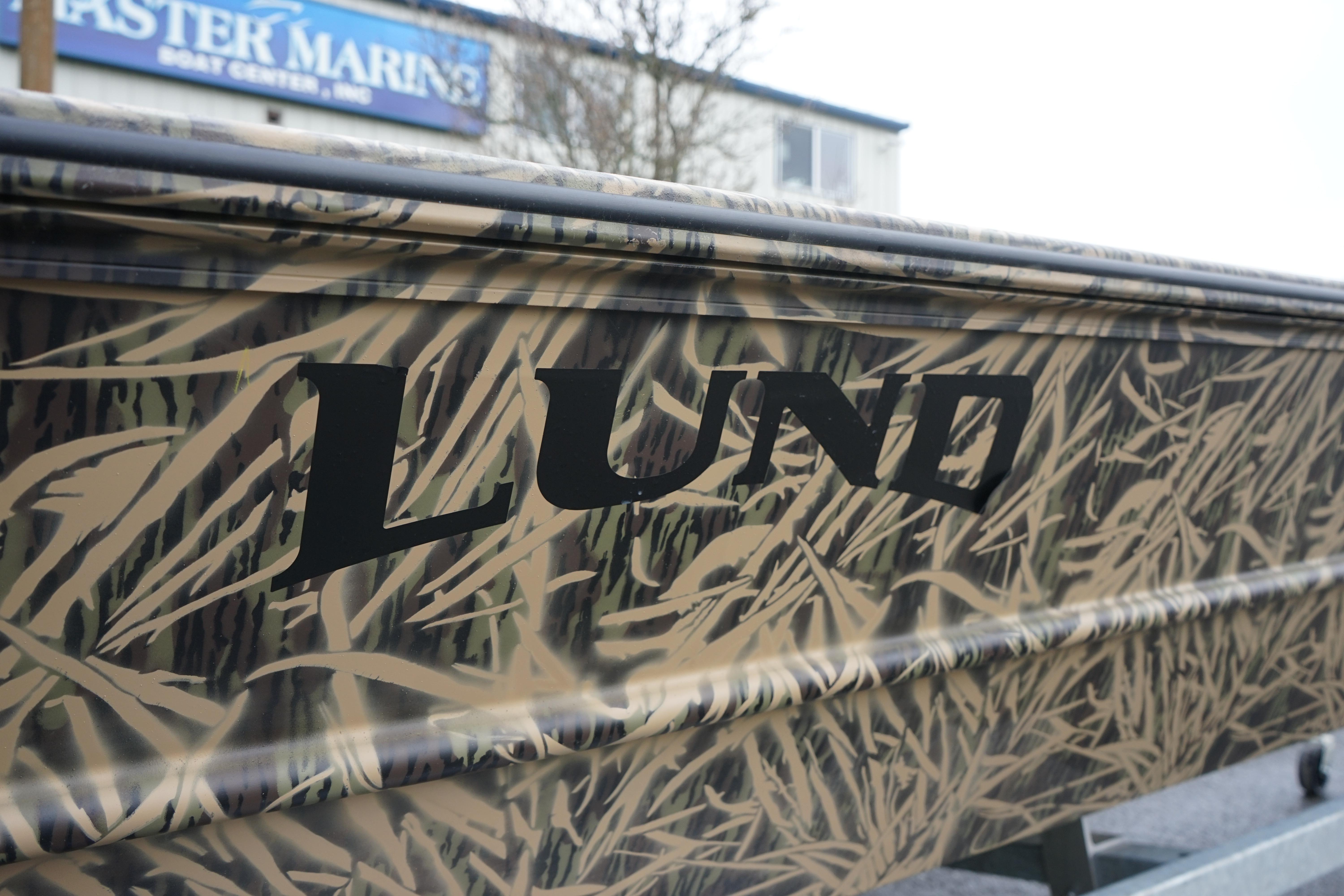 2024 Lund 1760 Predator Tiller boat with camouflage design at a marine center.